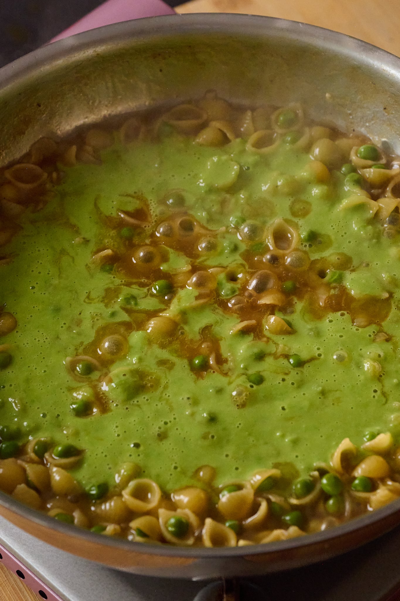 Large stainless steel pan has cooked pasta, peas and pea puree in it.