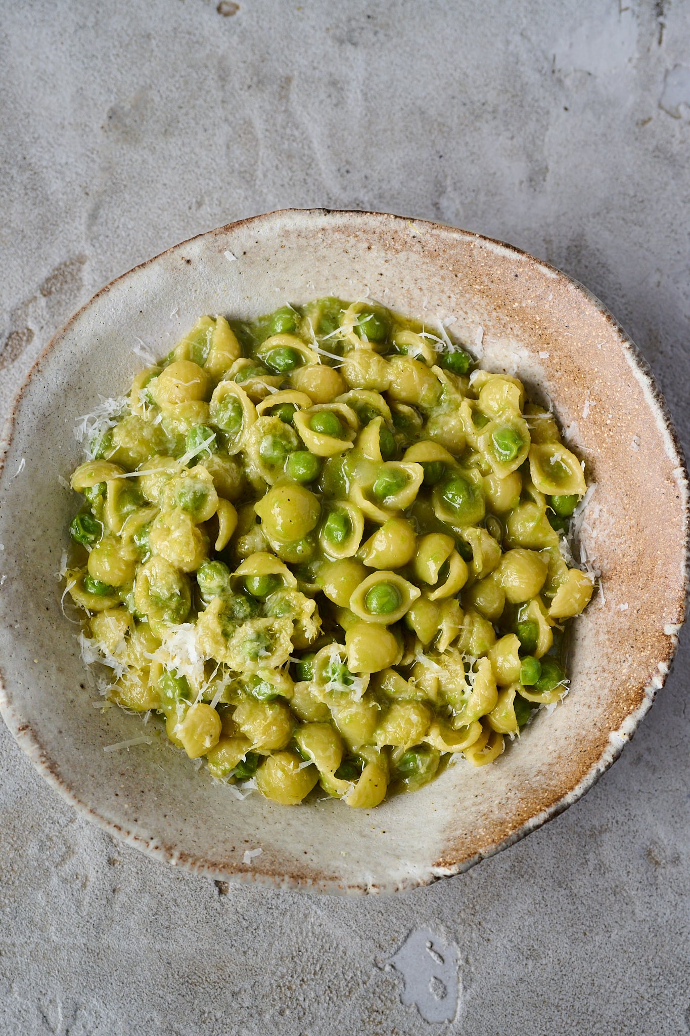 Pasta e piselli, pasta with peas, sits in brown bowl with parmesan grated over the top.