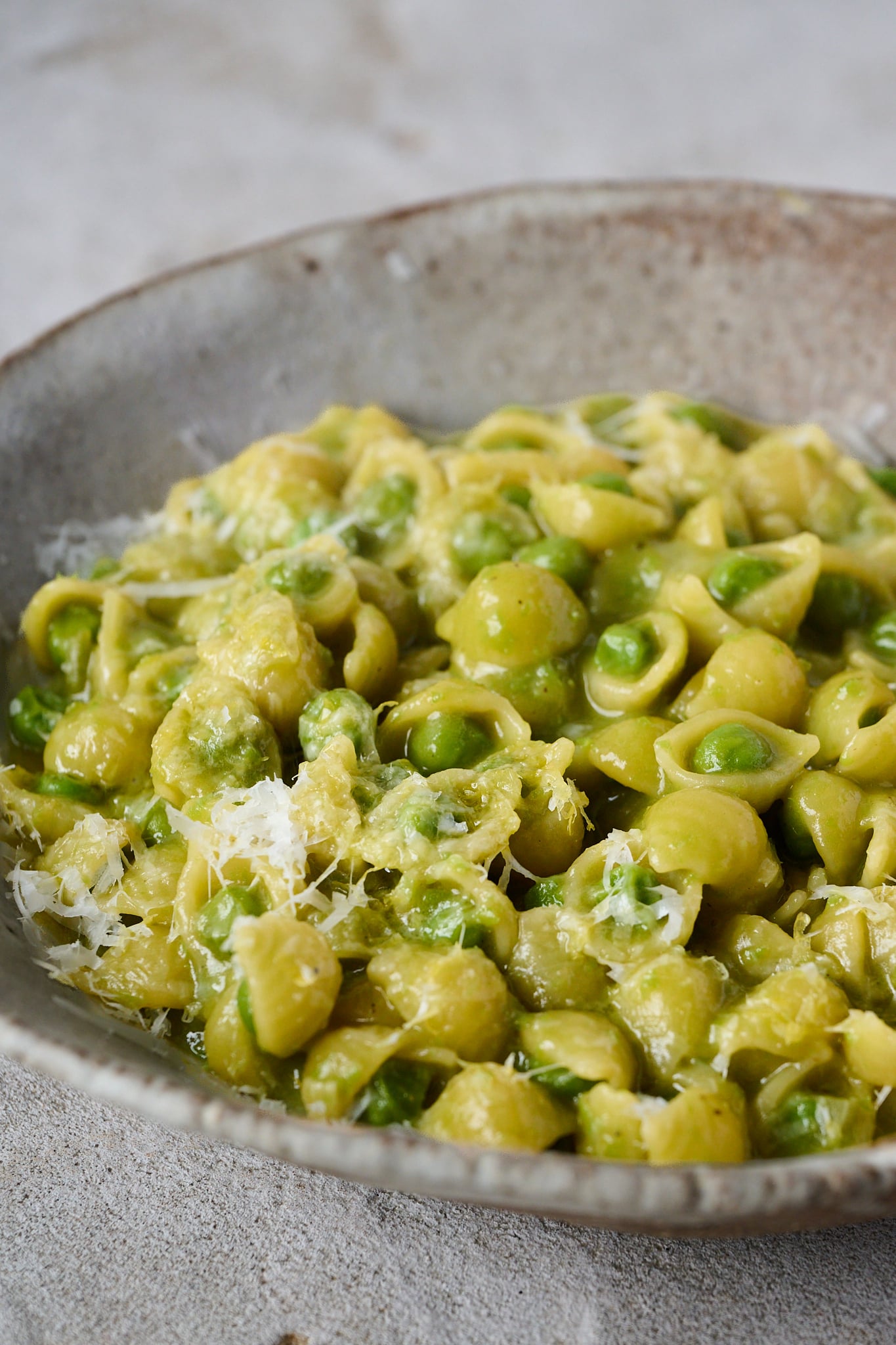 Pasta e piselli, pasta with peas, sits in brown bowl. 