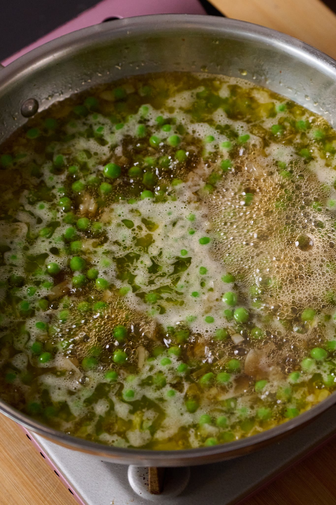 Large stainless steel pan is filled with peas, onions, garlic and stock.