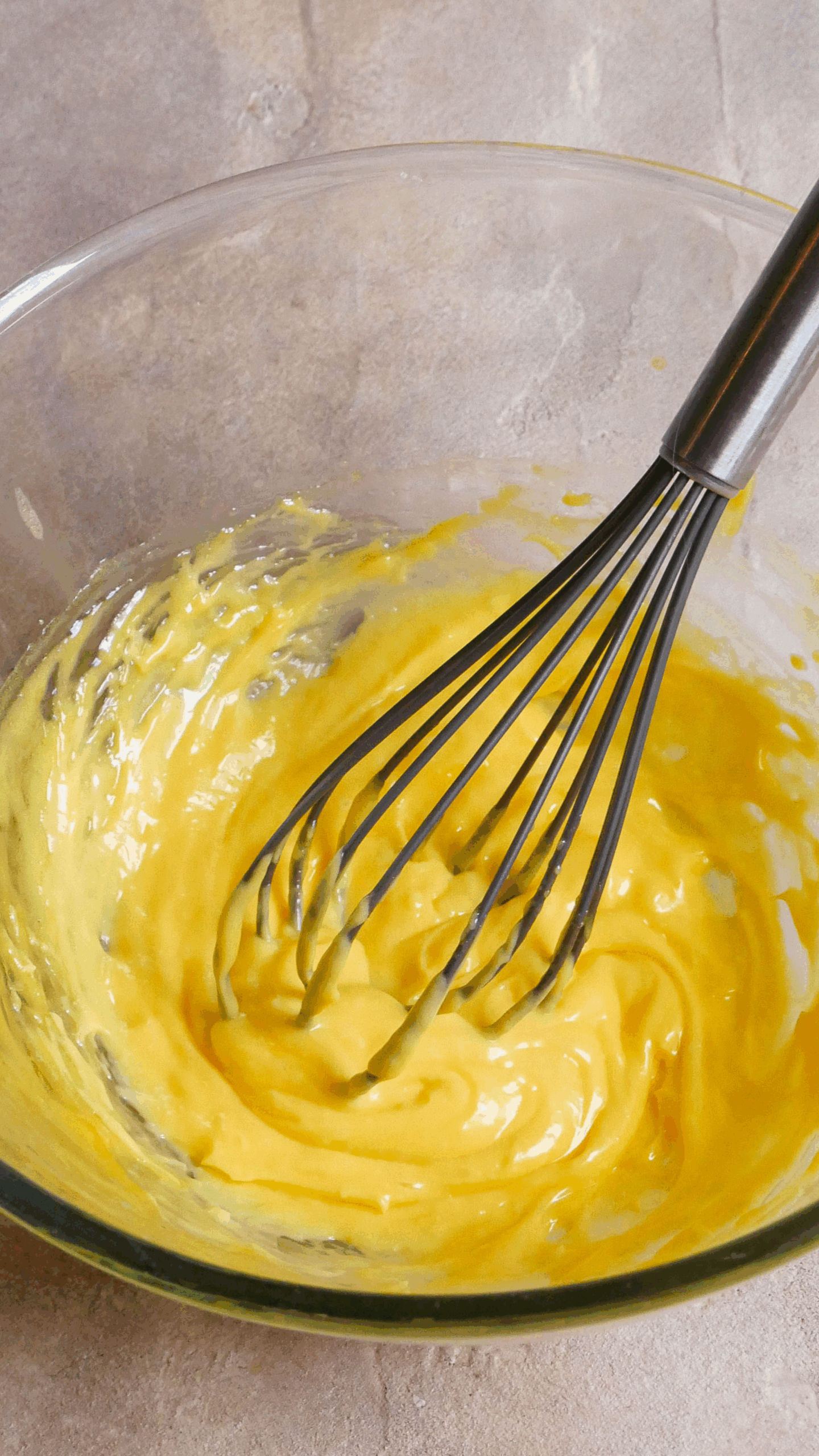 Hollandaise sauce sits in glass jar with a grey whisk sitting out the side. 