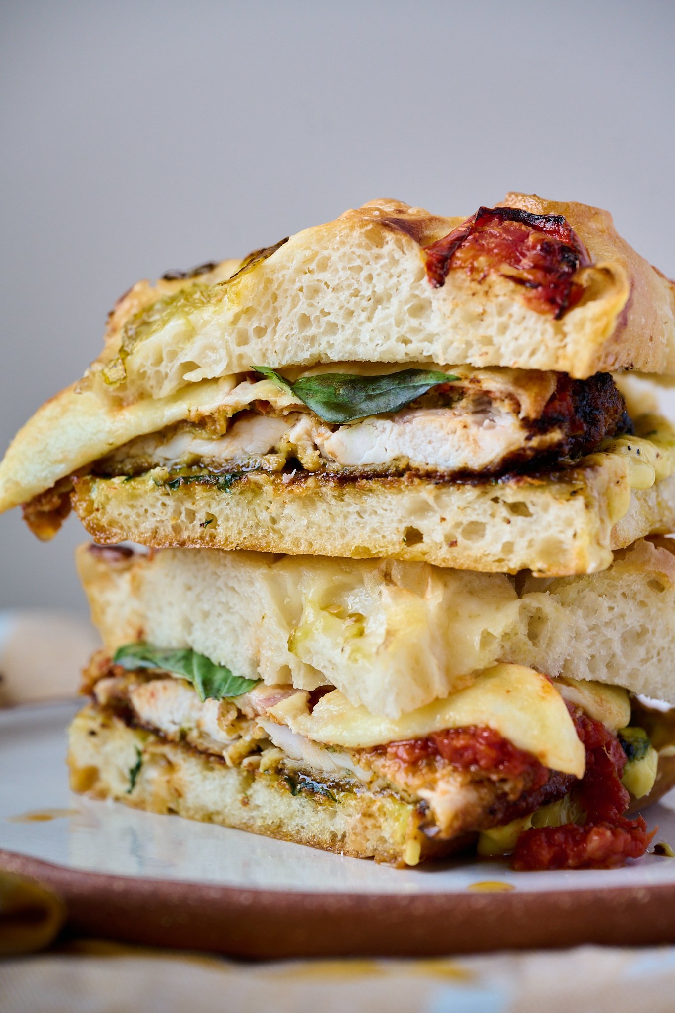 Chicken parm sandwich that has been sliced in half and is sitting on plate. You can see all elements of the sandwich in this photo.