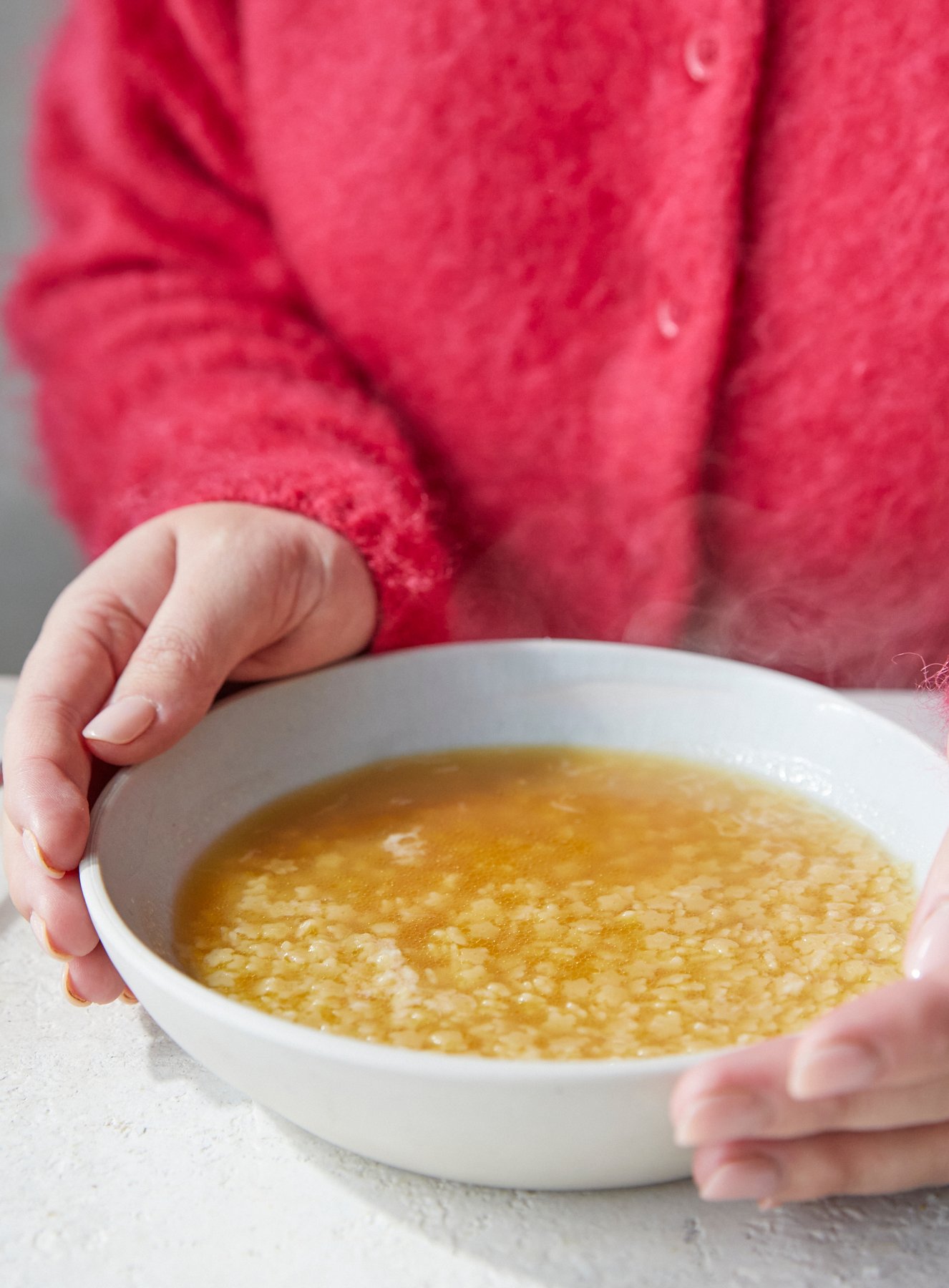 Pastina in chicken broth in a bowl is being hugged with someone in a pink fluffy jumper.