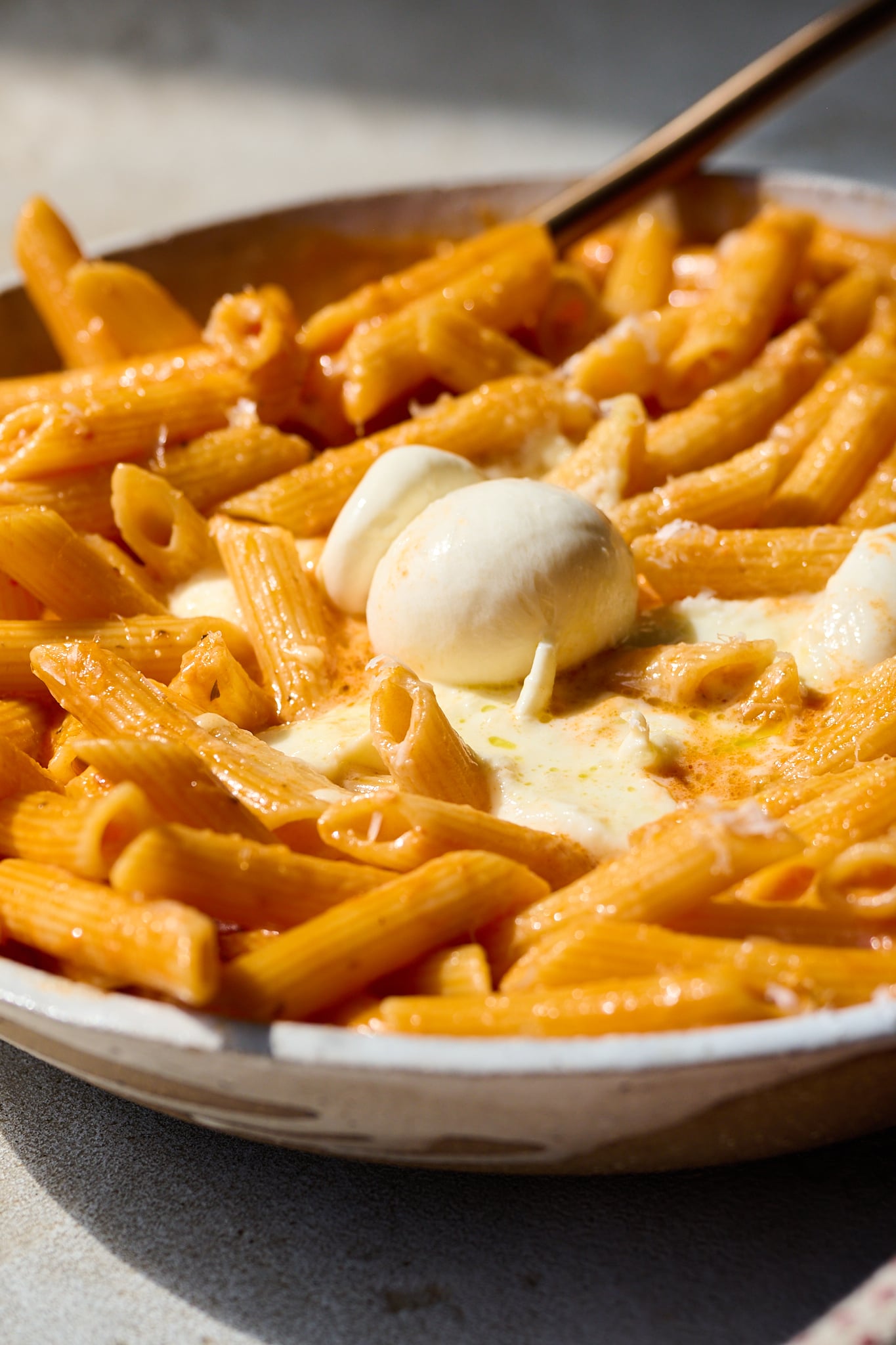 Pasta all vodka in large white bowl with burrata cracked open on top.