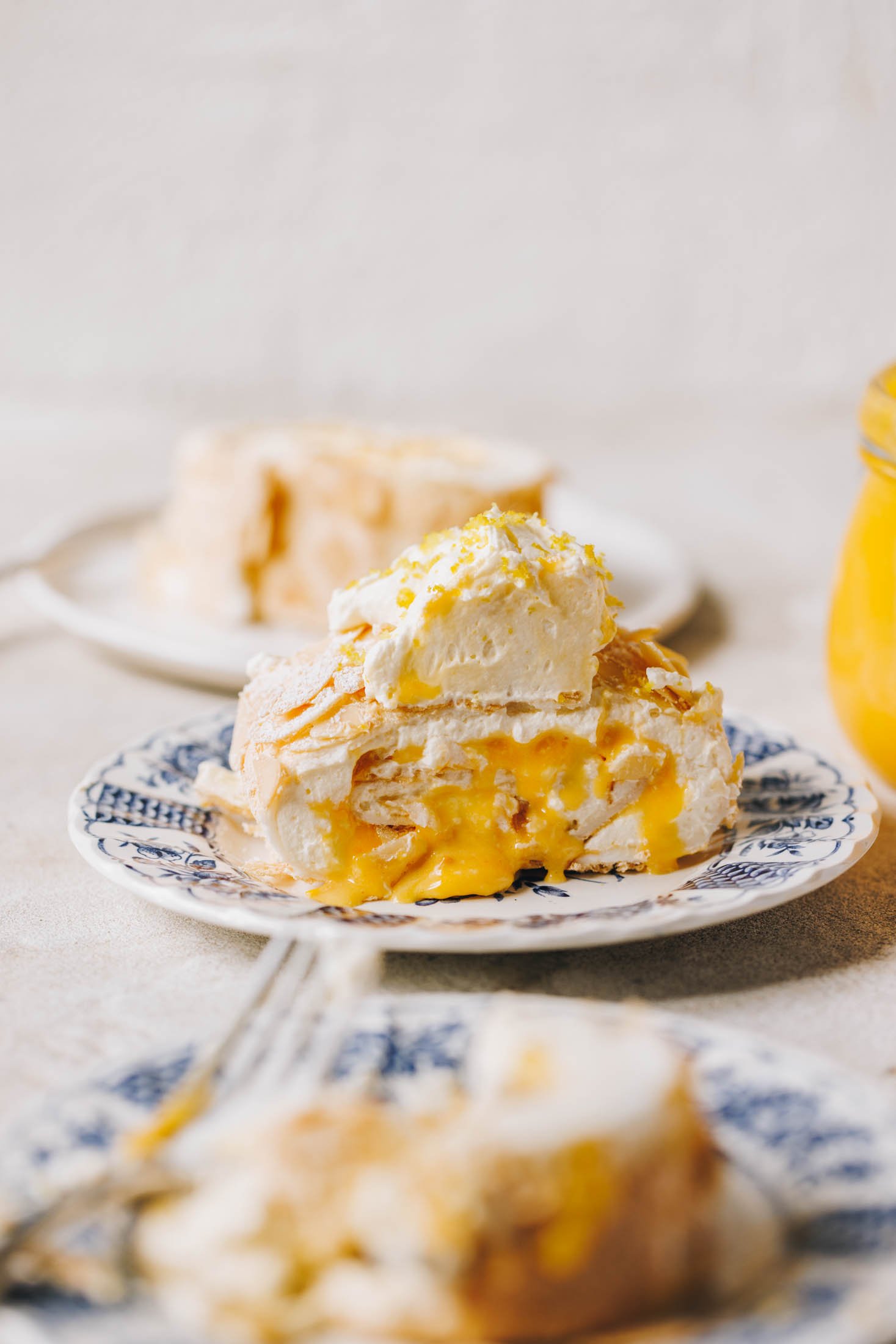 A slice of lemon curd meringue roulade sits on a blue and white plate with a floral pattern.