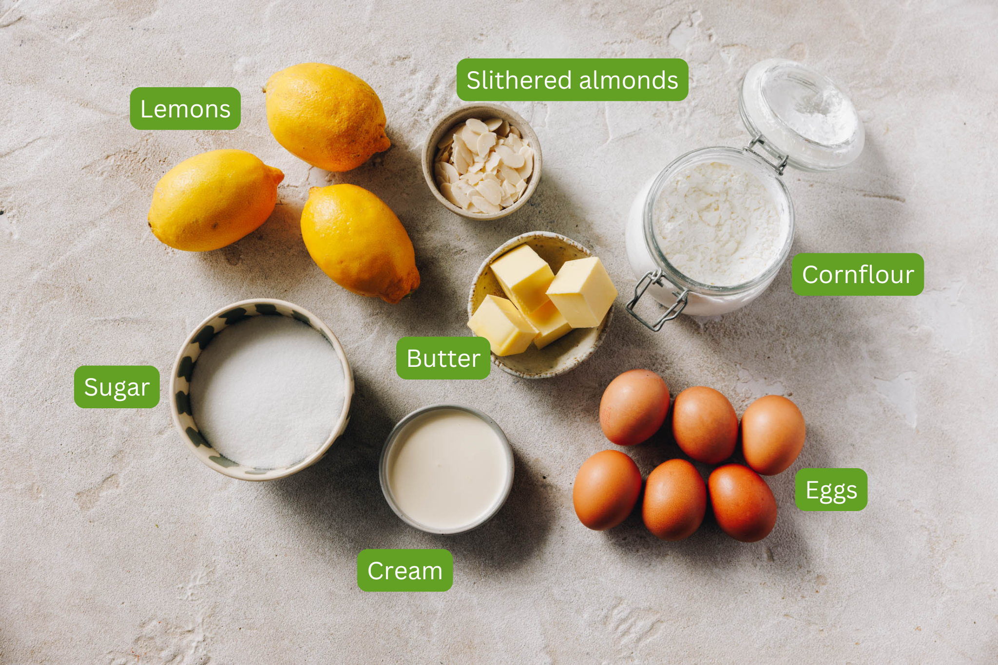 Image of ingredients needed for lemon curd meringue roulade. These include butter, cream, sugar, eggs, cornflour, almonds and lemons.