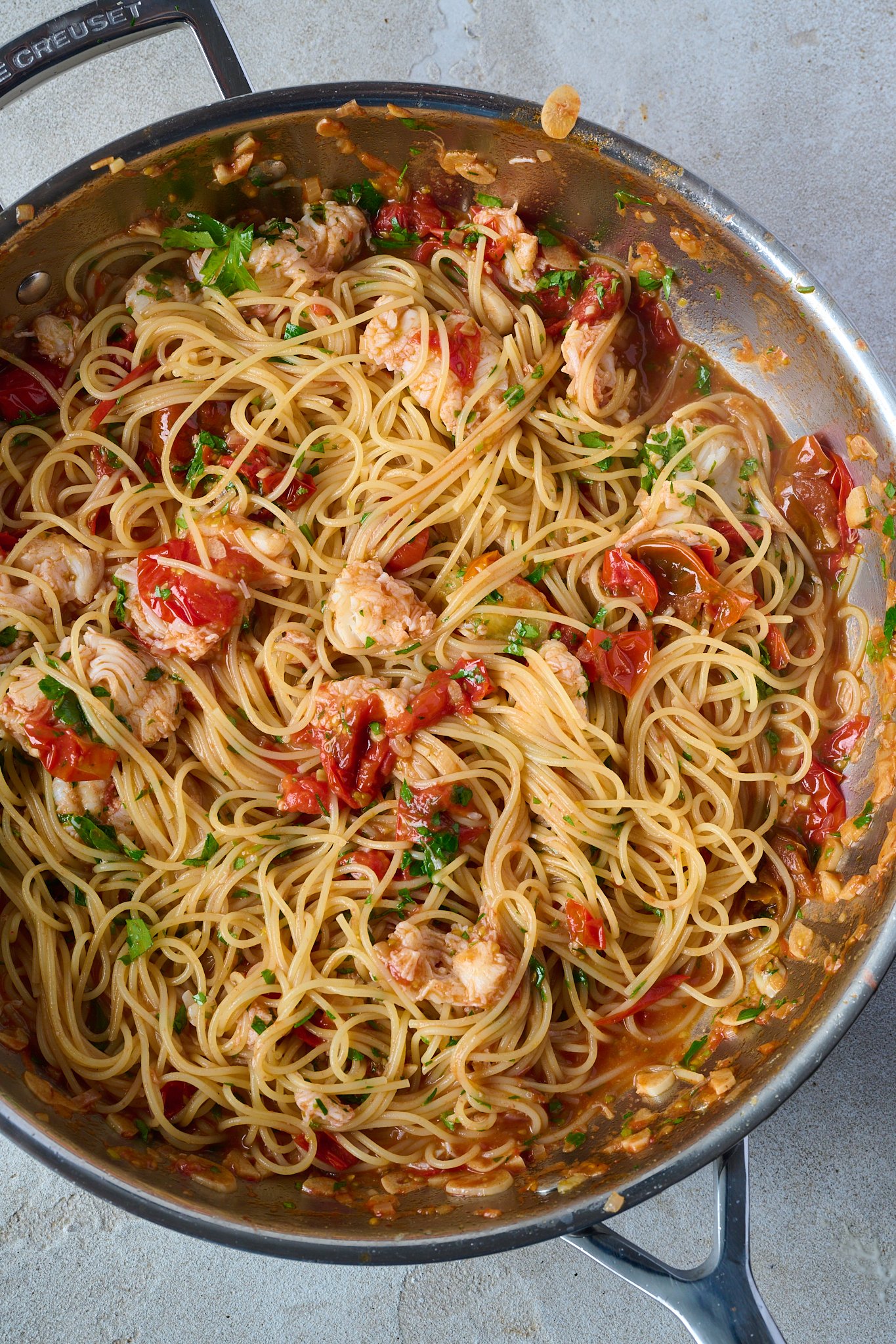 Buttered lobster pasta with cherry tomatoes sits in large frypan. It has been sprinkled all over with parsley.