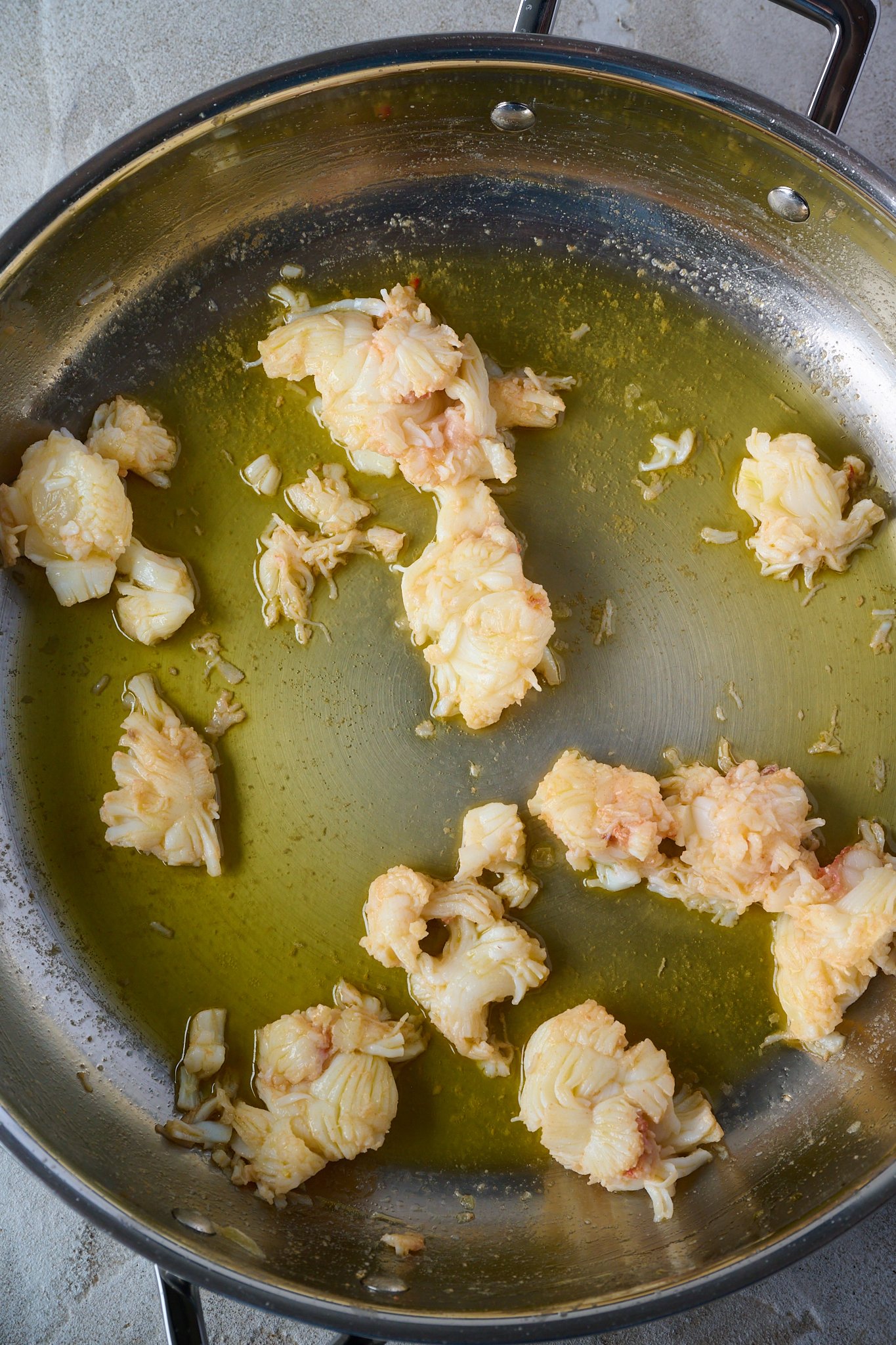 Lobster meat has been poached in butter and is sitting in large stainless steel fry pan.