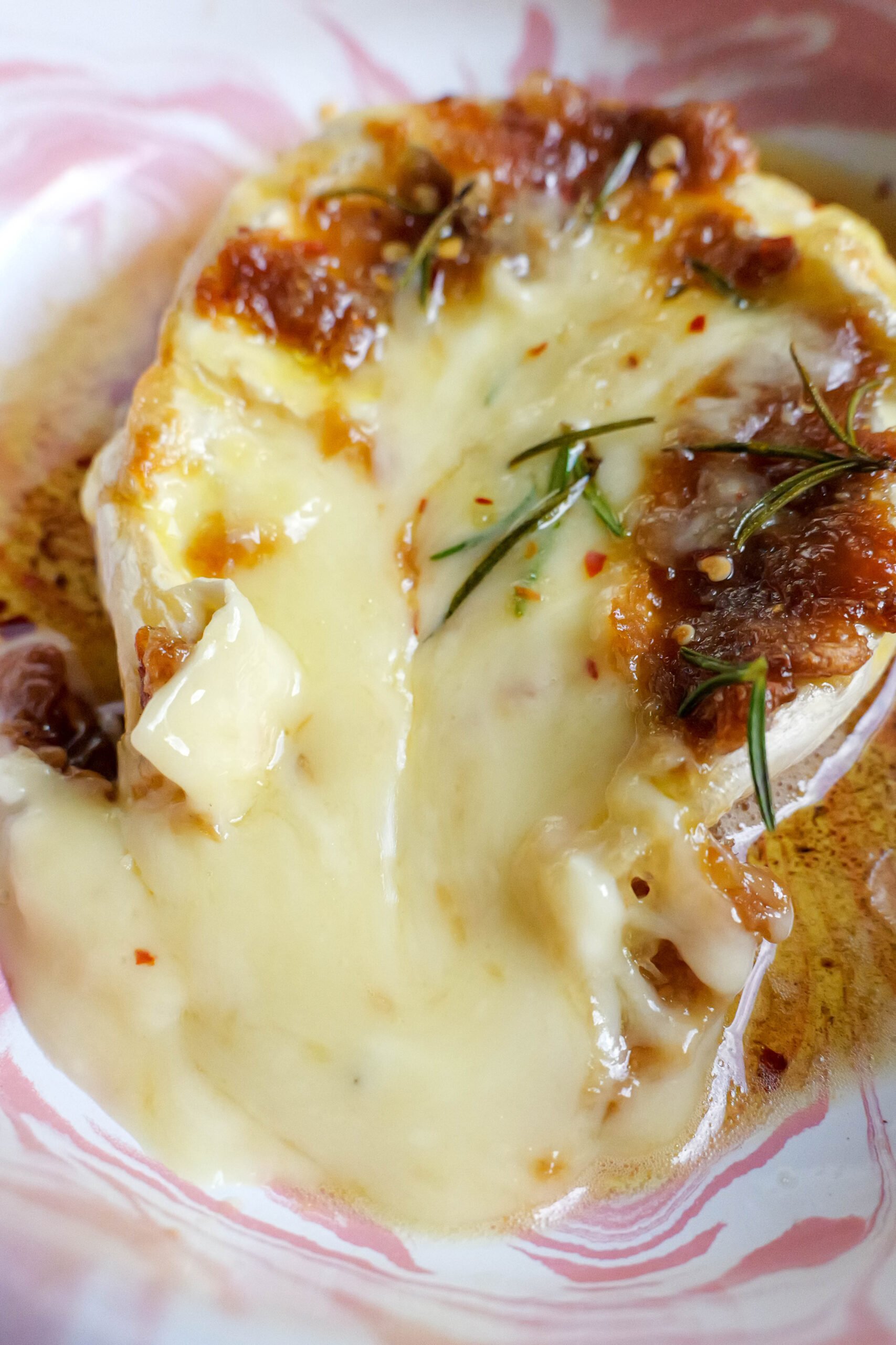 Baked brie with roasted garlic butter sits in pink and white tray. The brie has been cracked open and is oozing into the tray.