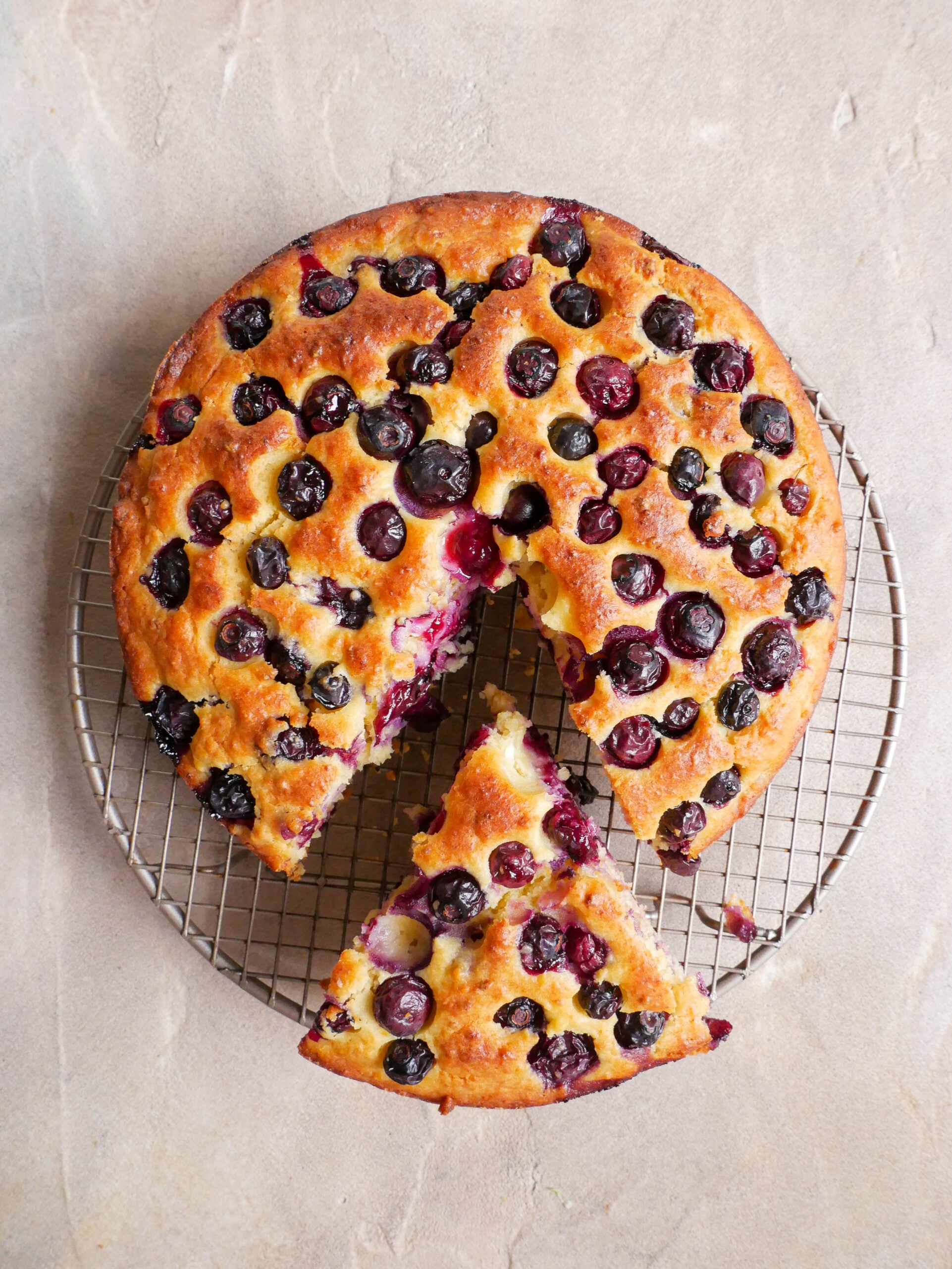 blueberry, Lemon & Ricotta Olive Oil Cake sits on wire cake rack.