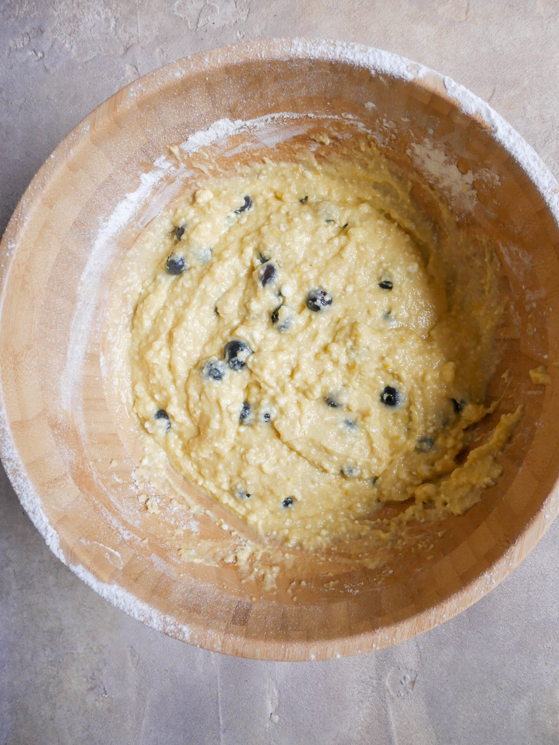 Large wooden bowl is filled with cake batter. You can see blueberries.