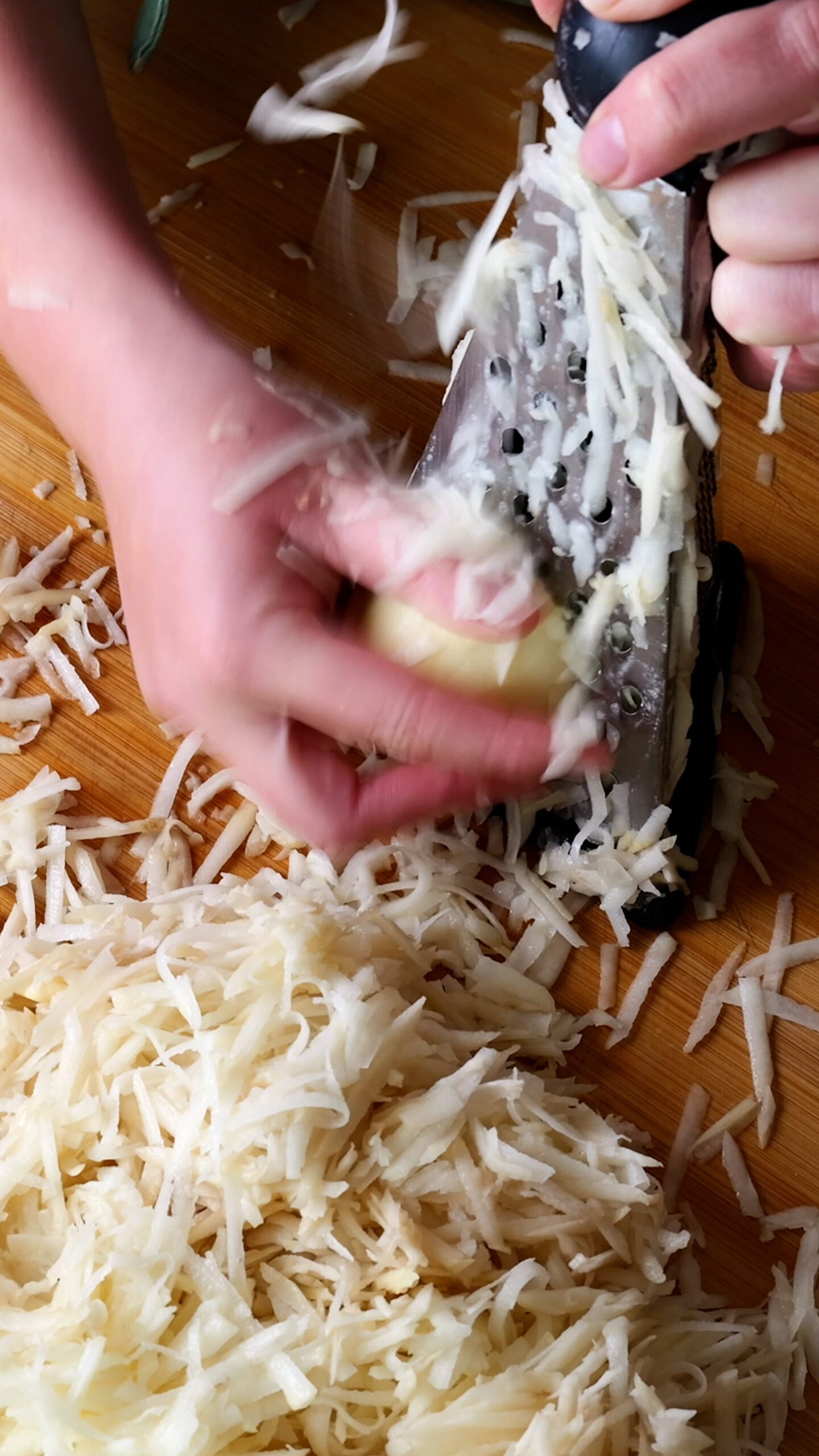 Potato is being grated on a cheese grater. 