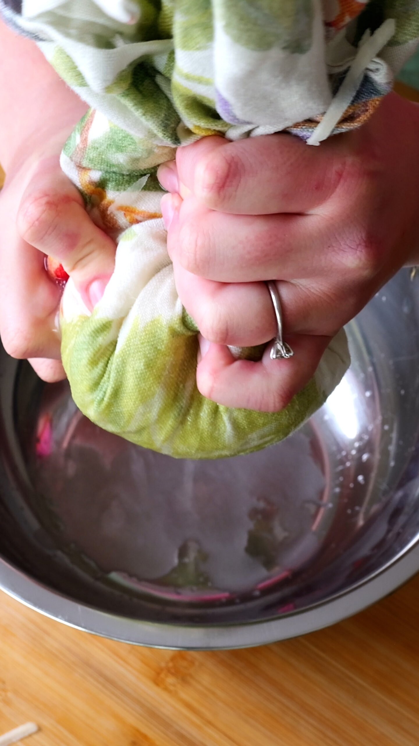 potatoes are in green tea towel and water is being squeezed out of them into metal bow. 