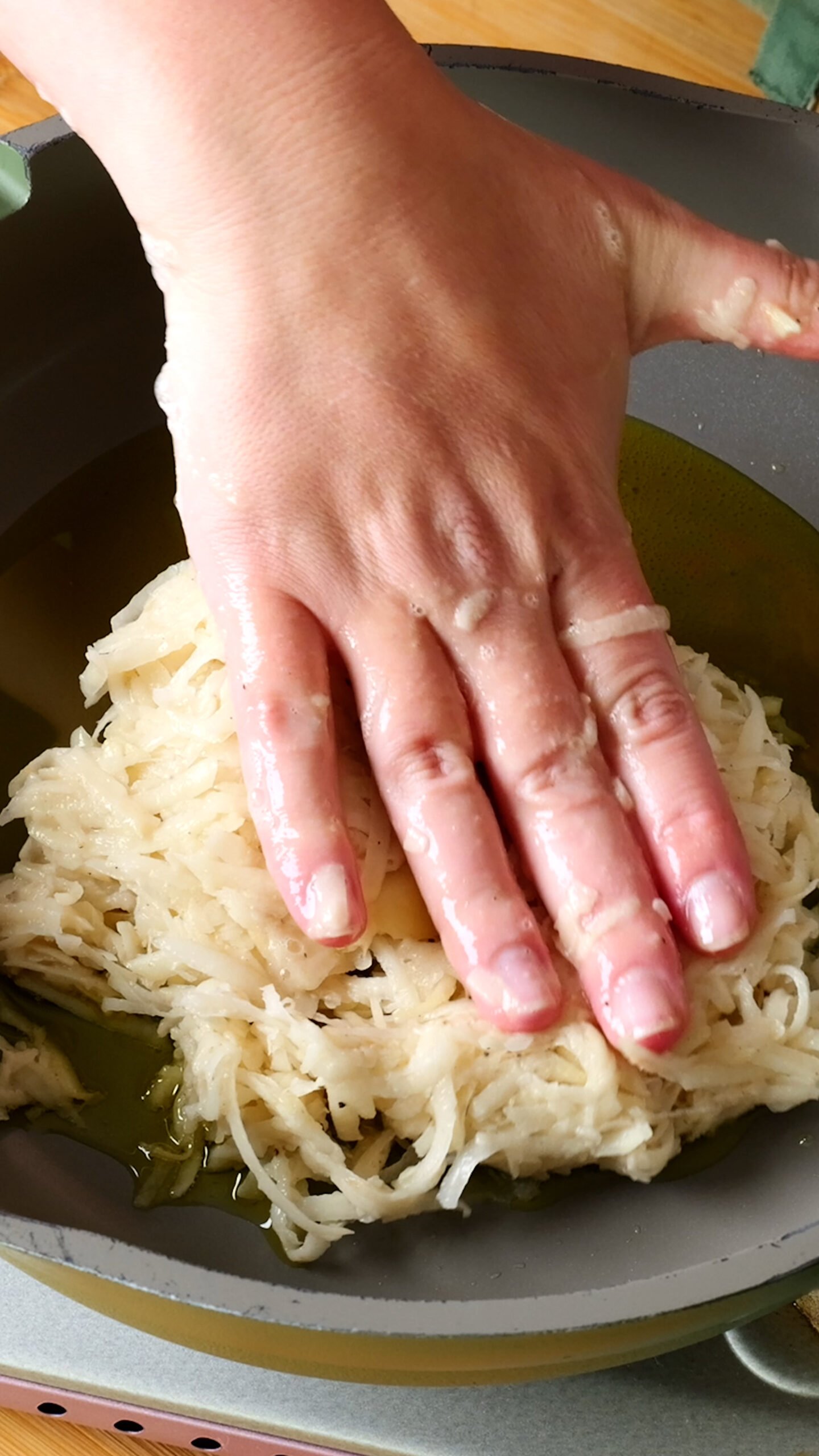 grated potato is being pushed into pan with olive oil in it. 