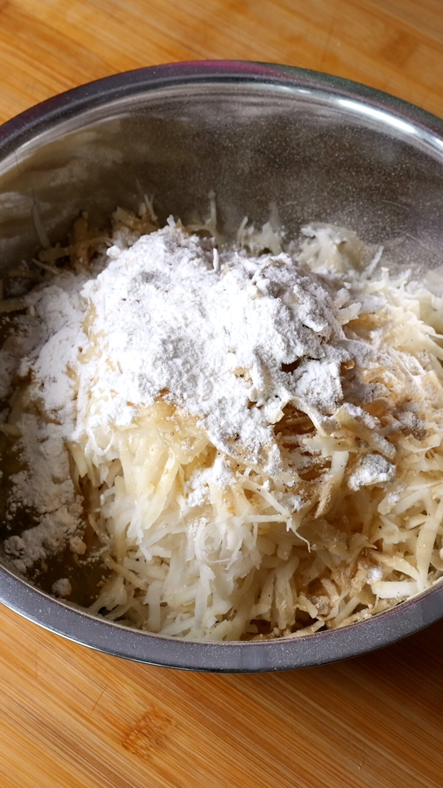Grated potatoes are in metal bowl and have all seasoning over them. You can see lots of white flour