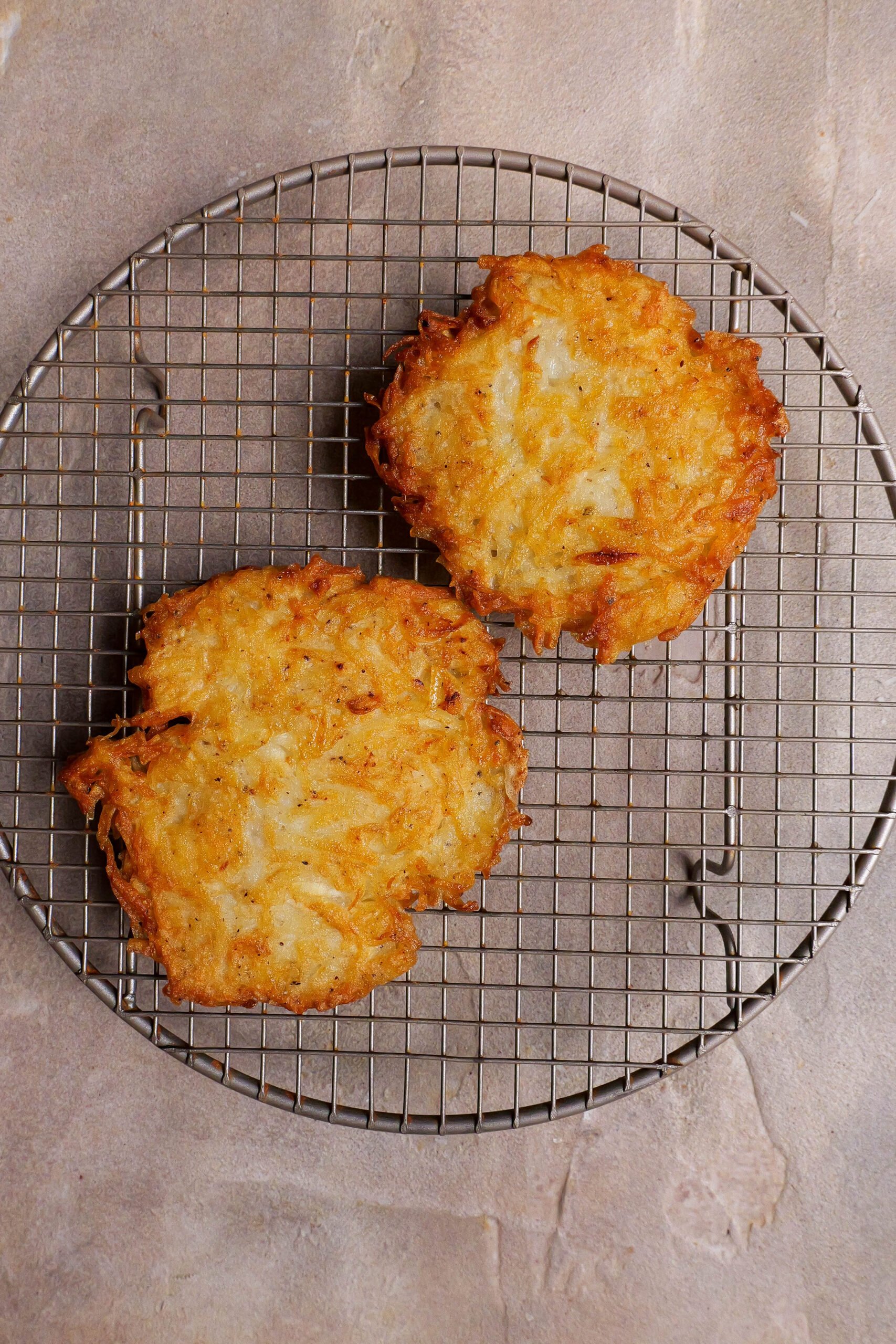 Potato rosti sit on a circular wire cooling rack.