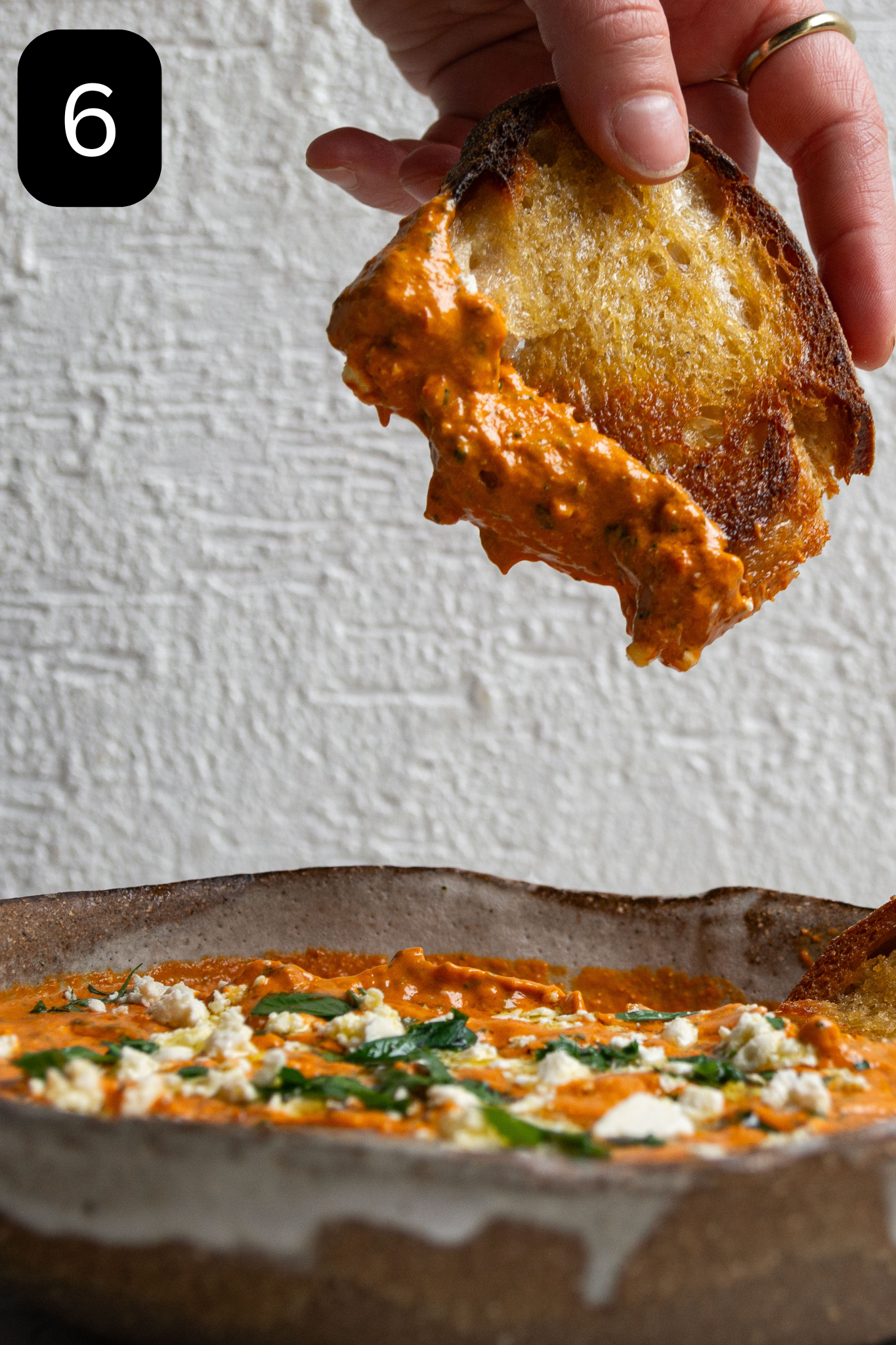 A piece of bread is being held and dipped into the bowl of dip. 
