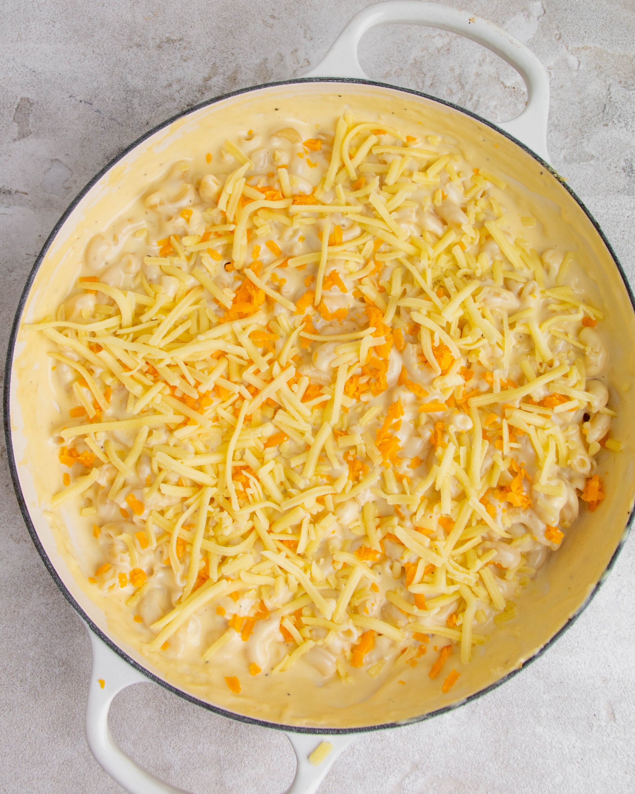 Baked mac and cheese with garlic confit is in large white baking tray and has cheese sprinkled all over. 