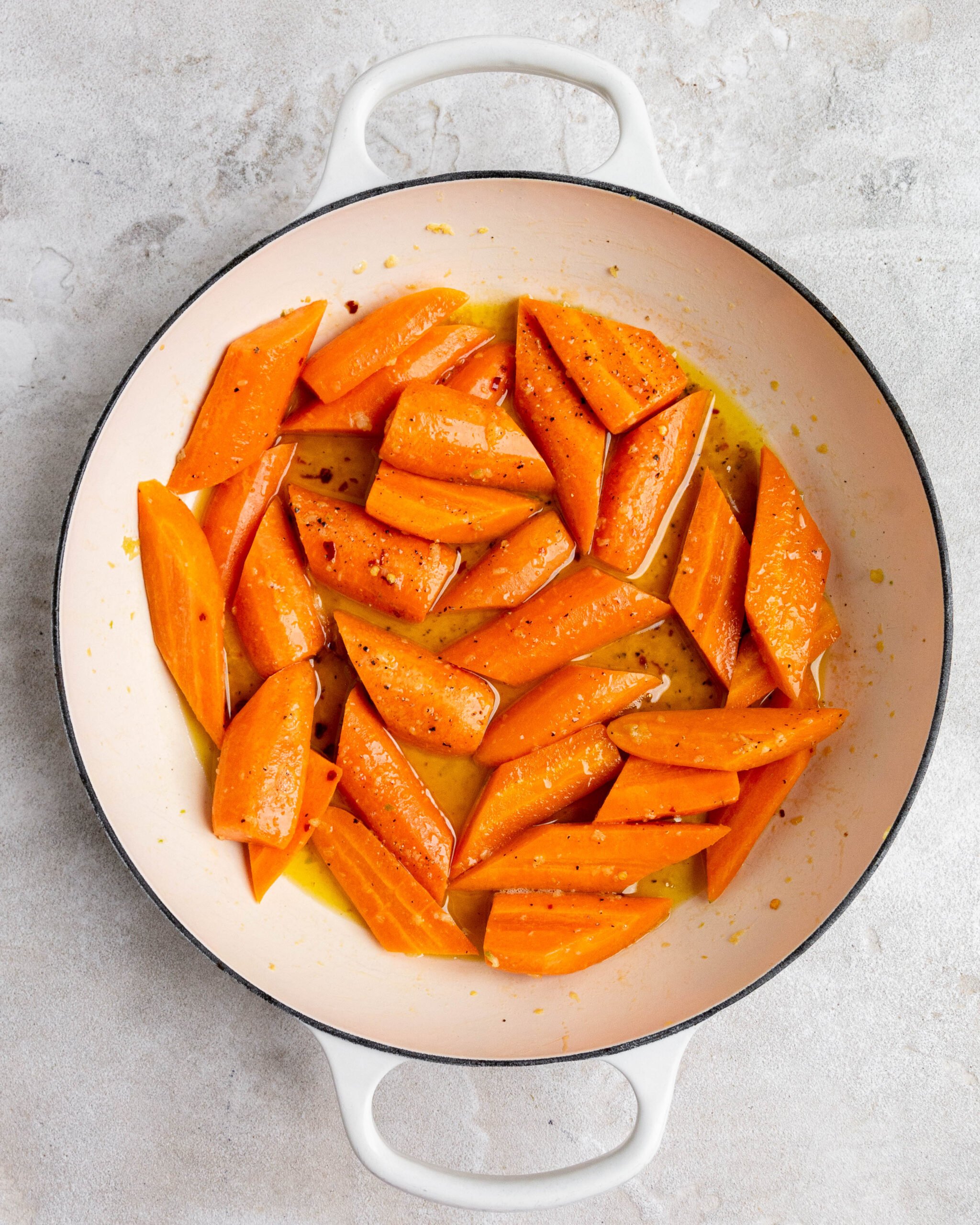 Sliced and peeled carrots sit in large white roasting pan with butter and honey. 