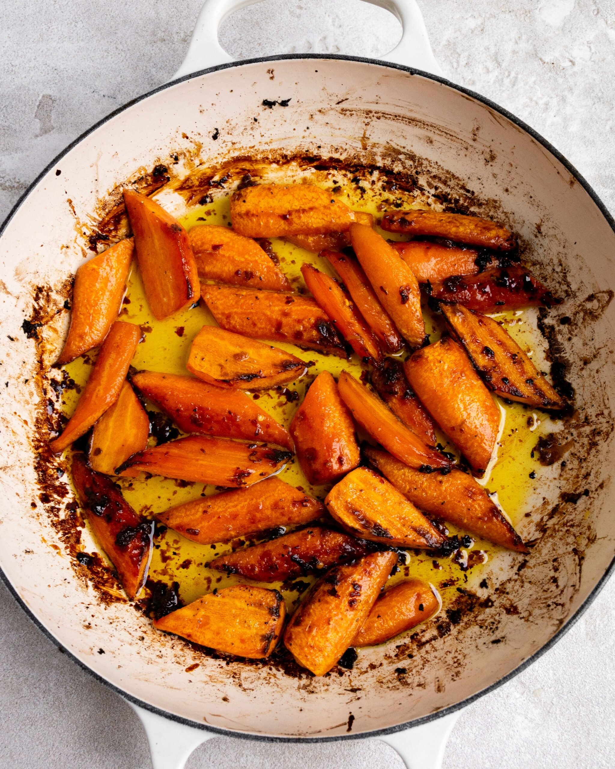 Sliced and peeled carrots sit in large white roasting pan with butter and honey. They have been roasted. 
