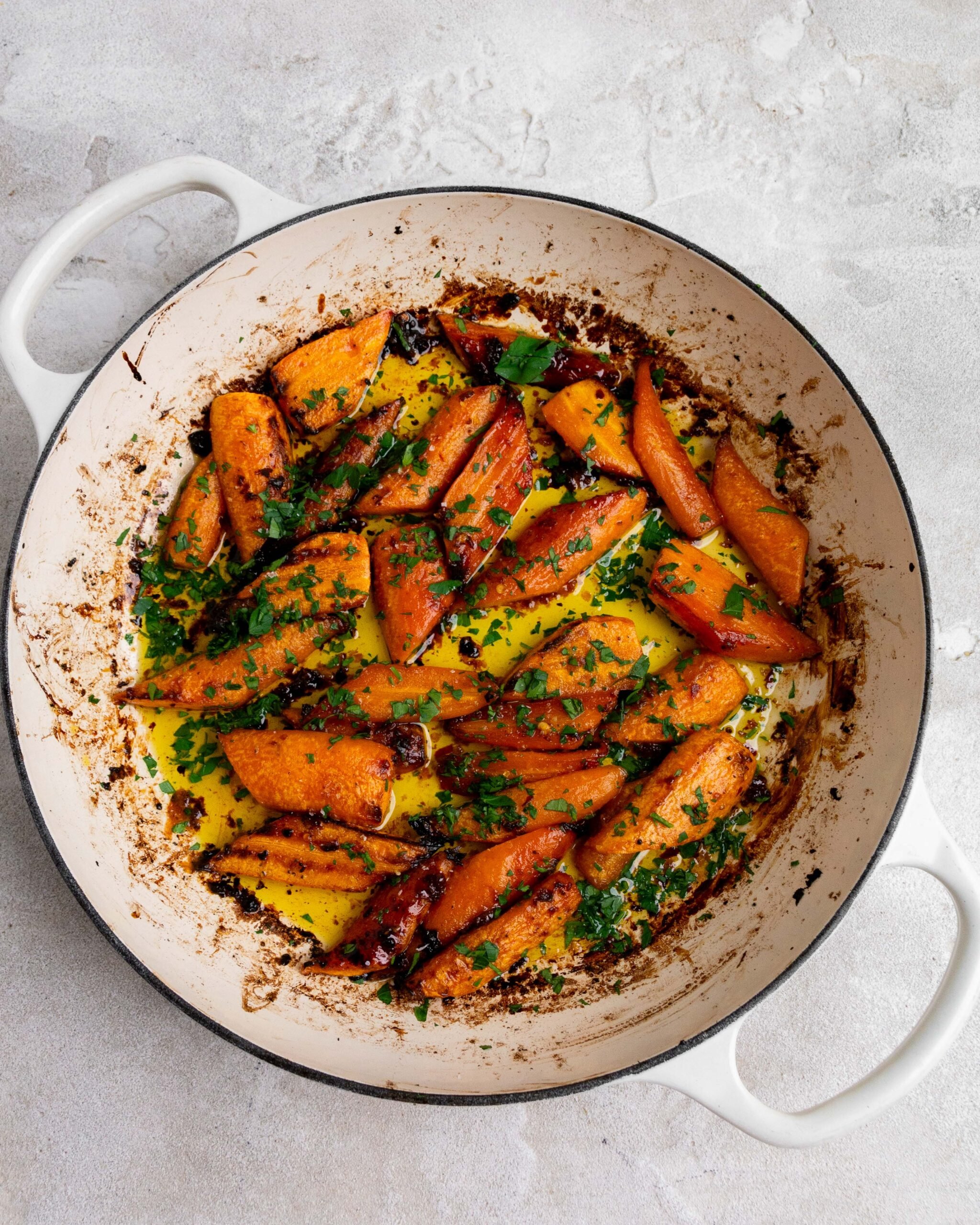 Sliced and peeled carrots sit in large white roasting pan with butter and honey. They have been roasted and been garnished with fresh parsley.