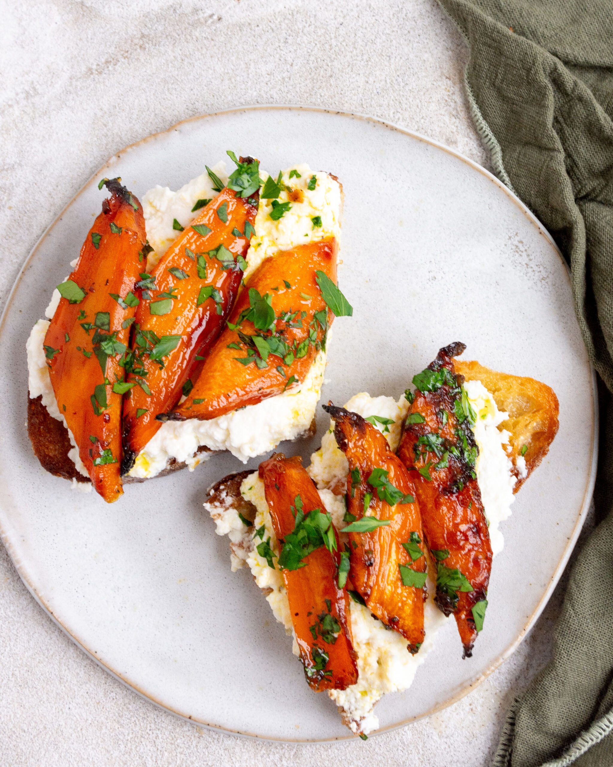 Hot honey roasted carrots sit on toast with ricotta. They are on a small white plate. 