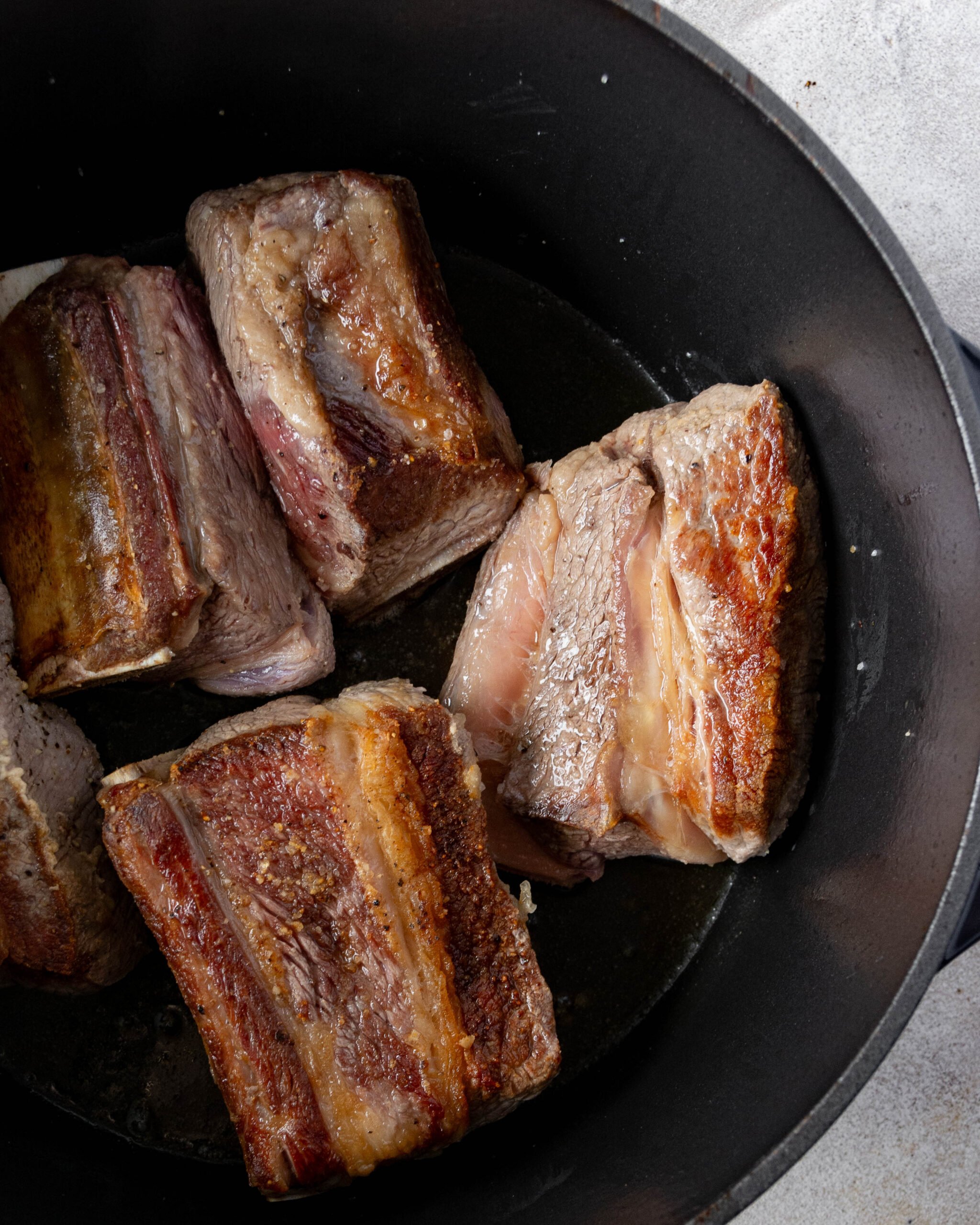 Seared beef short ribs sit in black pot. 