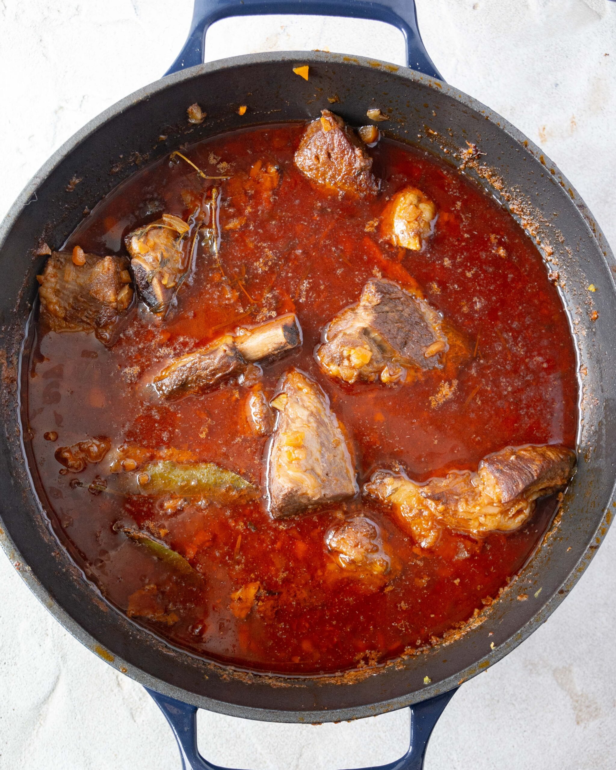 A big black pot is filled with a rich red sauce. You can see slow cooked beef short ribs poking out of the pot. 