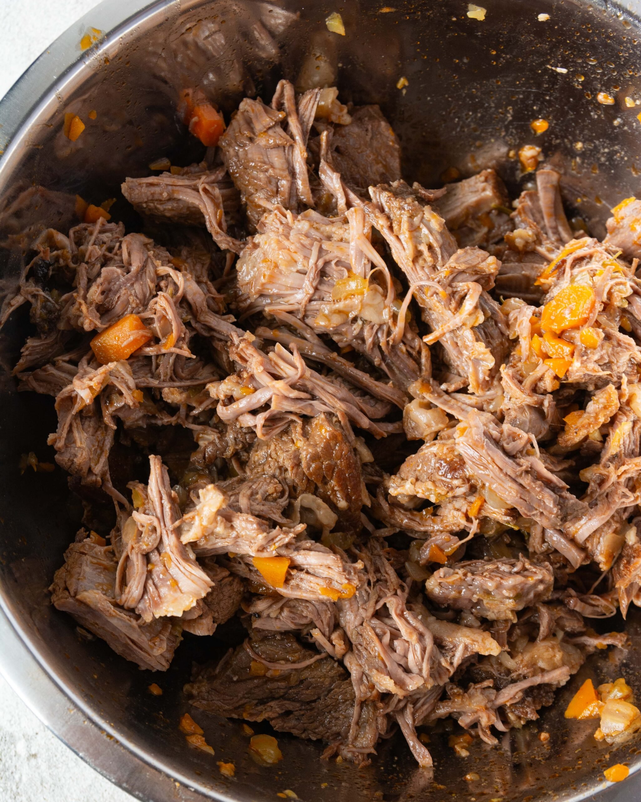 A metal bowl if filled with shredded meat. 