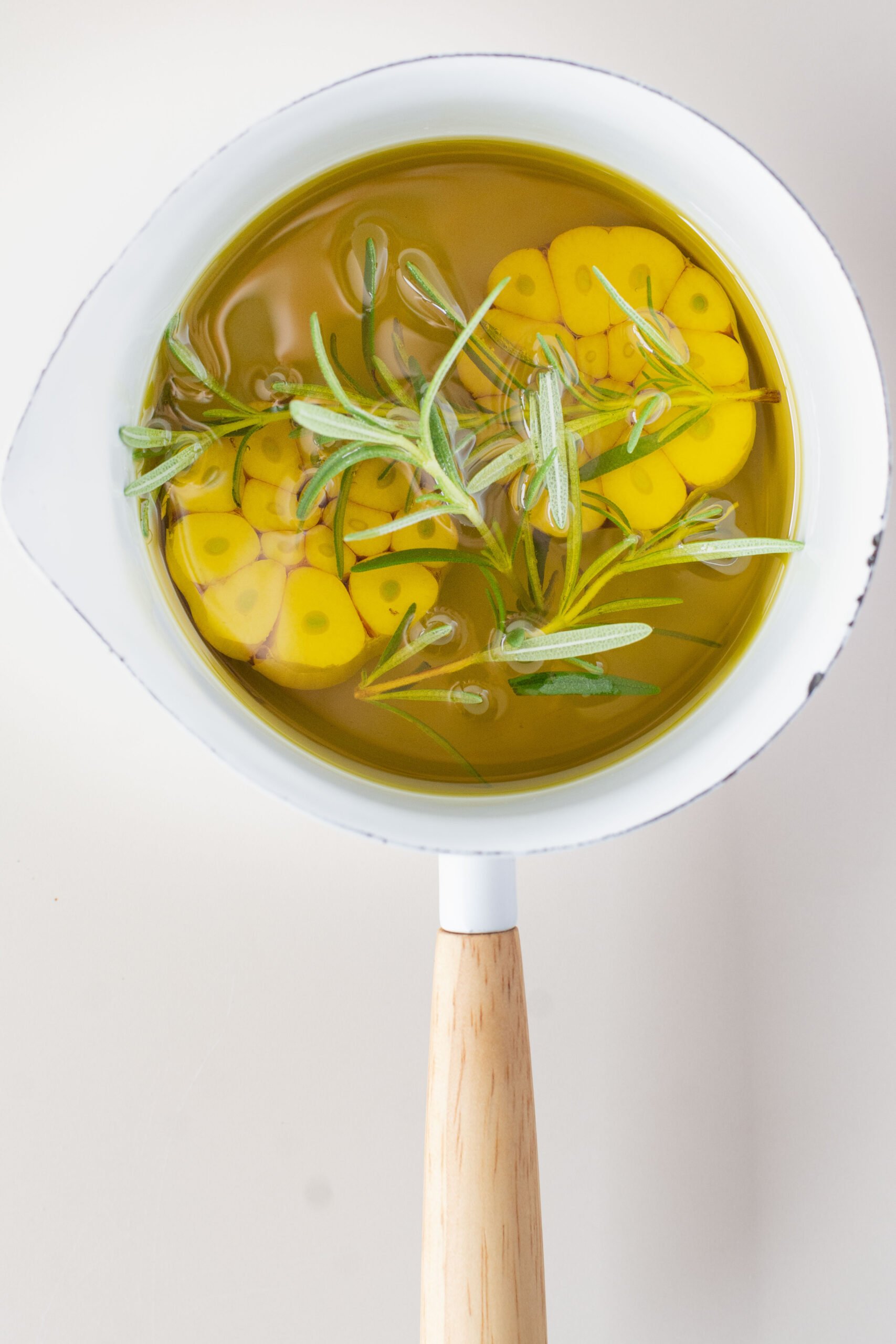 small white pot with oil, raw garlic and rosemary.