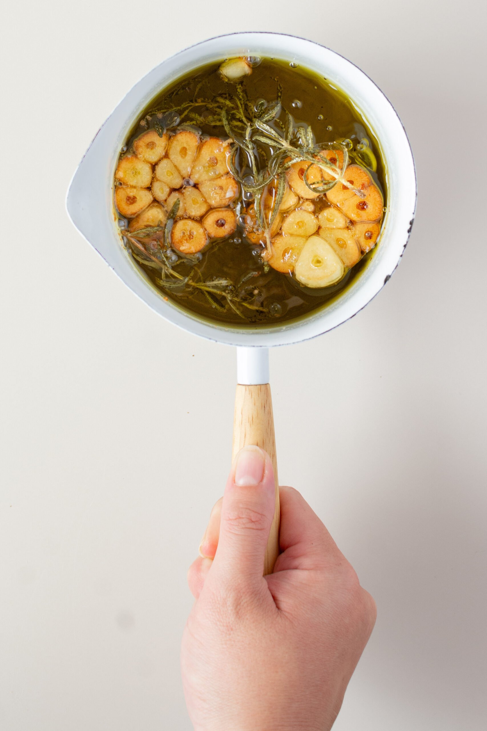 small white pot with oil, cooked garlic and rosemary.