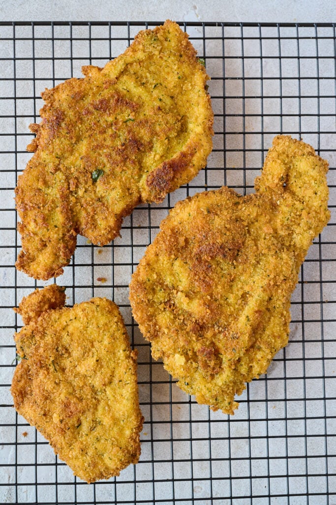 Three pieces of crispy breaded chicken laying on cooling rack. 