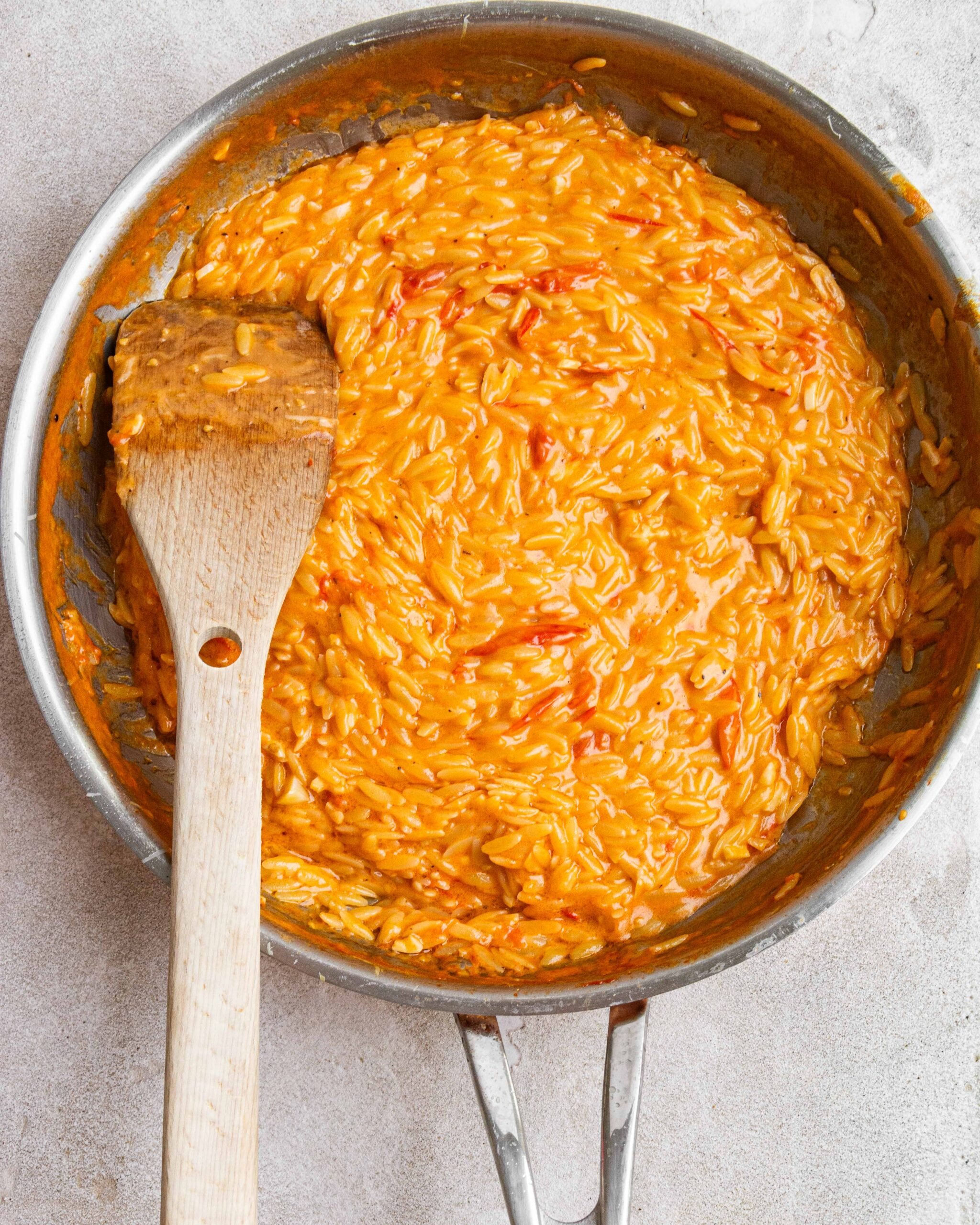 cooked orzo is in stainless steel pan with wooden spoon out the side.