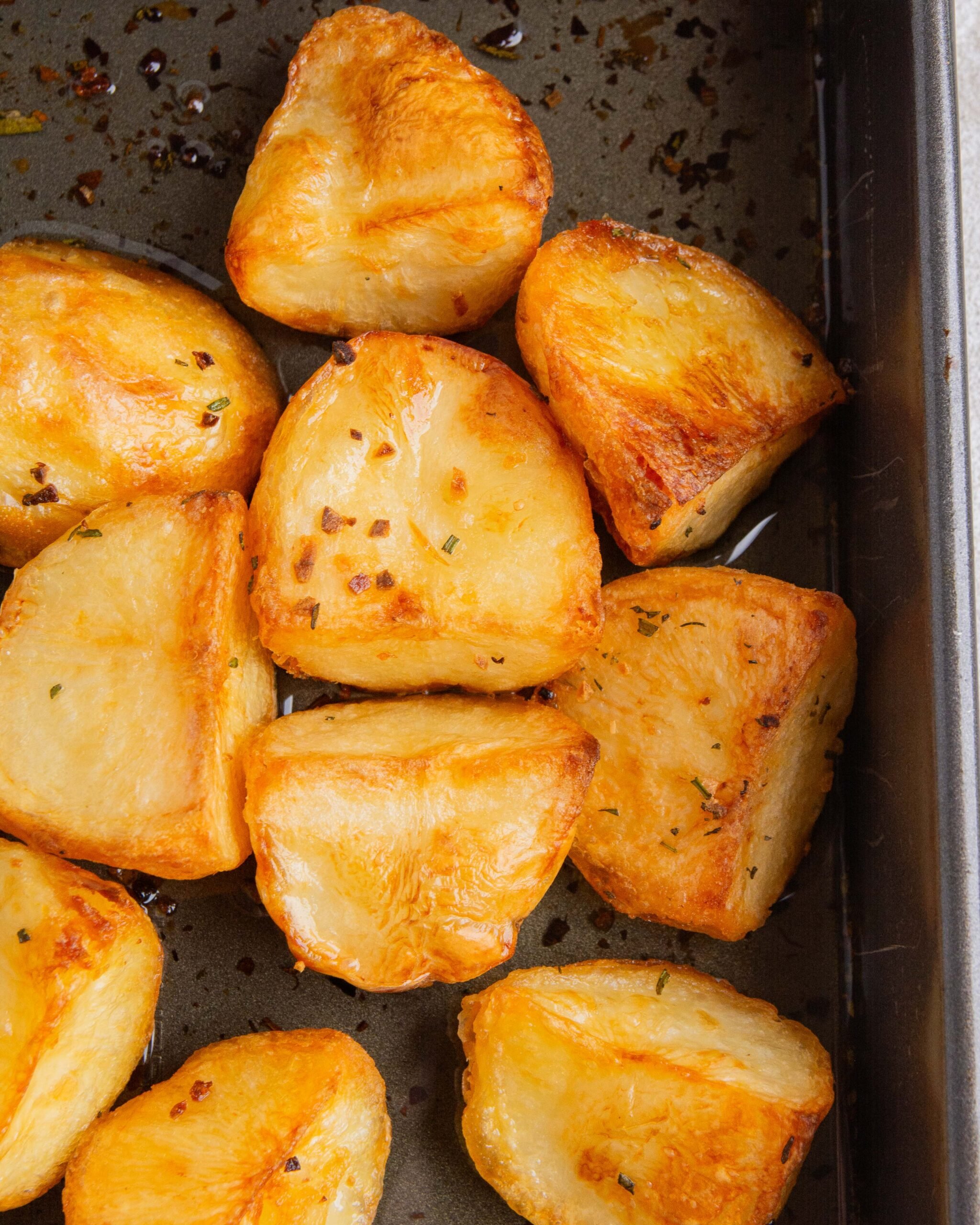 Crispy duck fat roasted potatoes sit in baking tin.