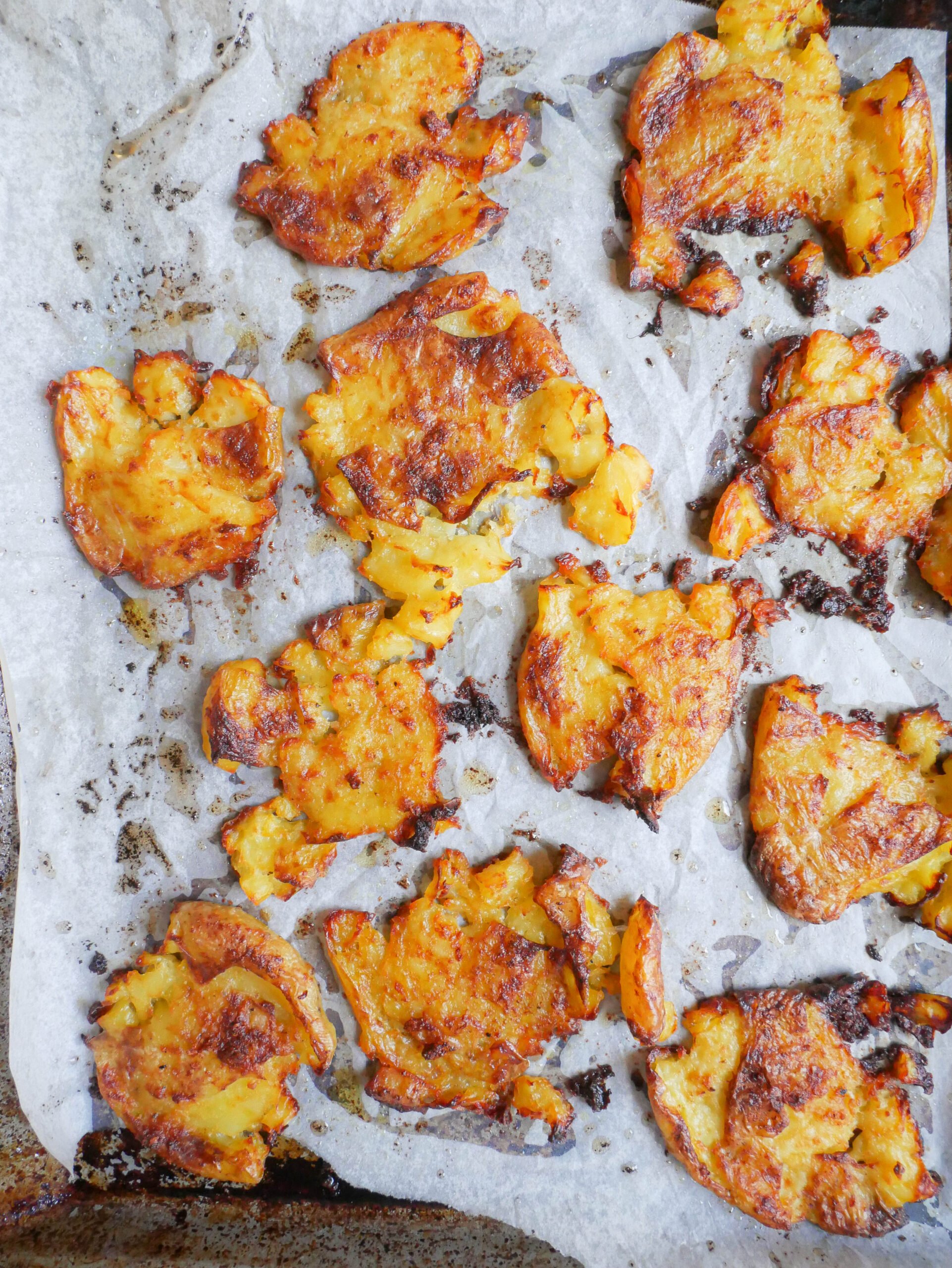 Crispy garlic butter smashed potatoes are on lined baking tray.