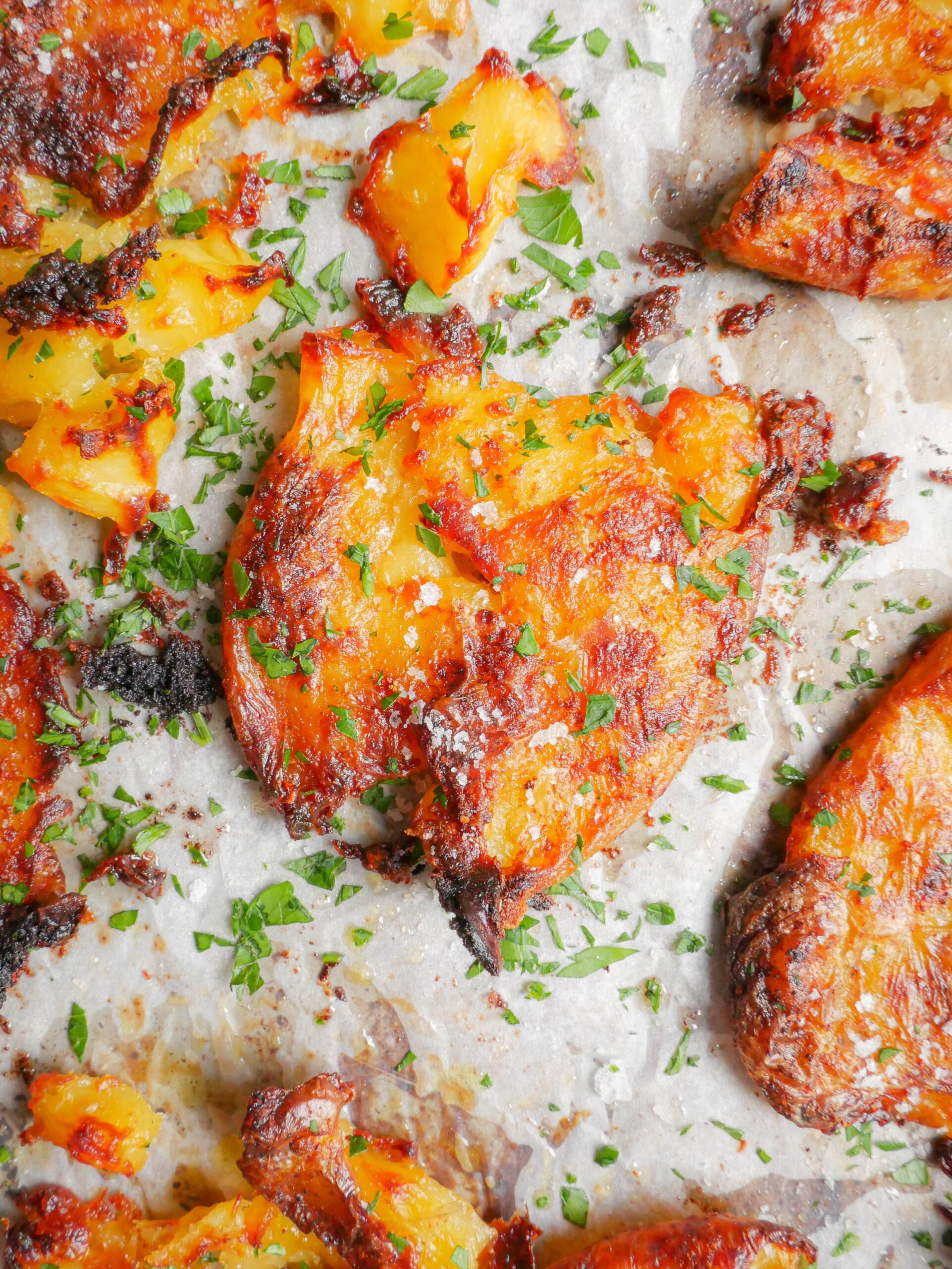 Crispy garlic butter smashed potatoes are on lined baking tray with parsley sprinkled all over.