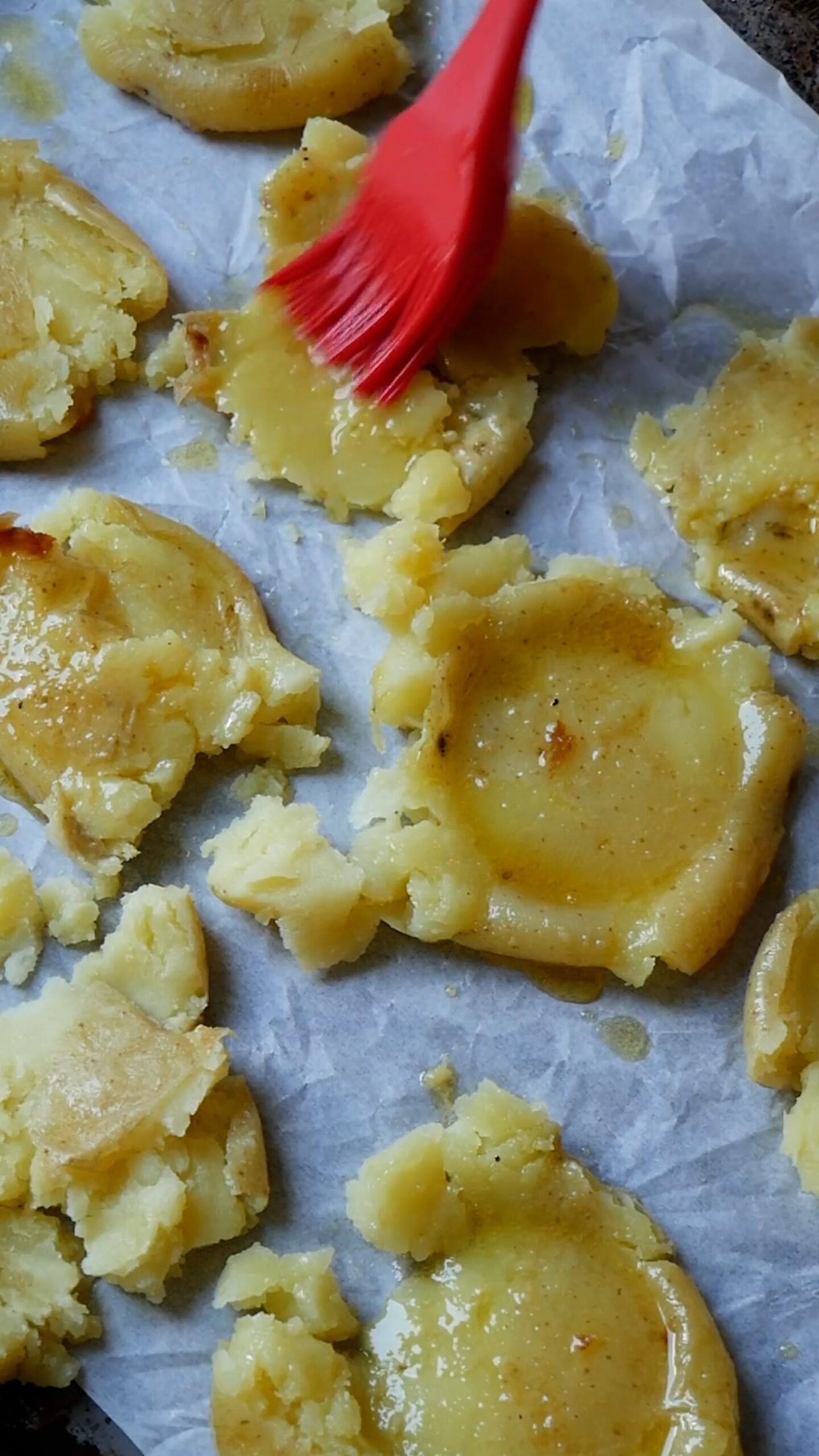 Smashed potatoes are being brushed with garlic butter.