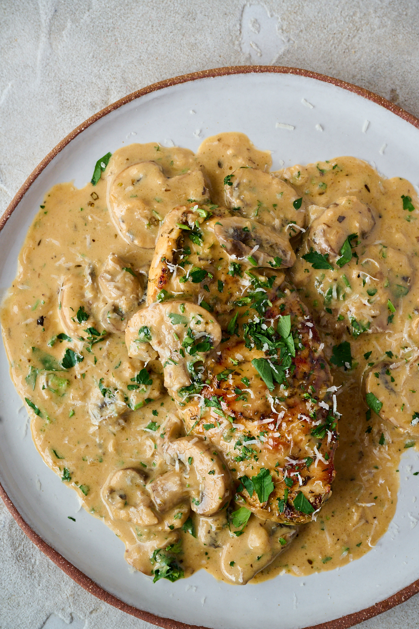 Pan seared chicken breast on plate with creamy mushroom sauce poured over and parsley sprinkled over the top.