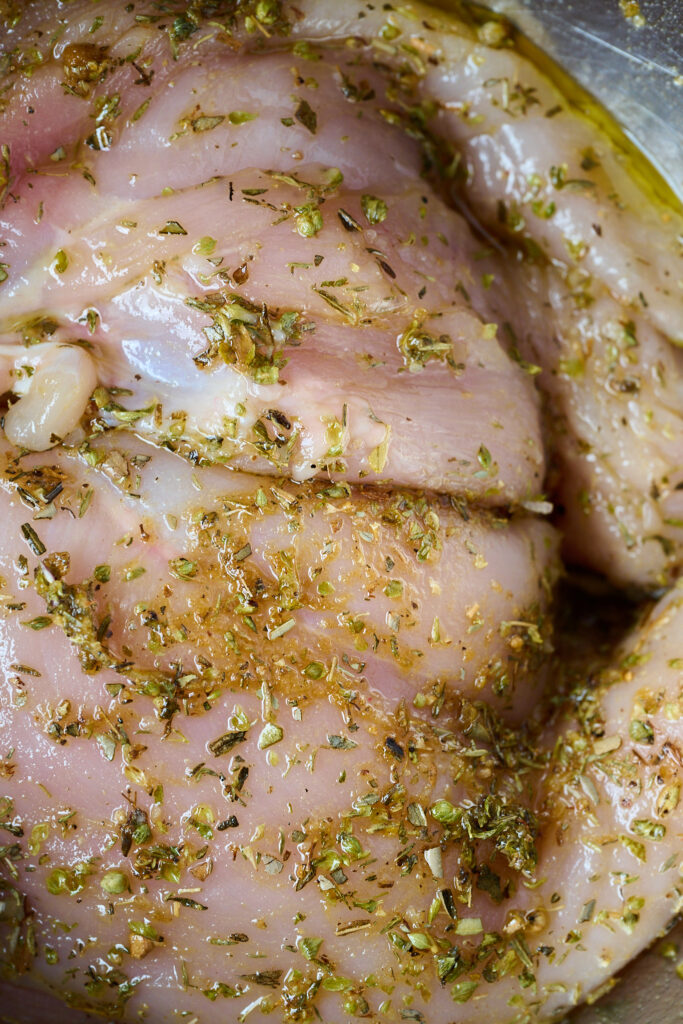 Raw chicken seasoned in spices and laying in large bowl.