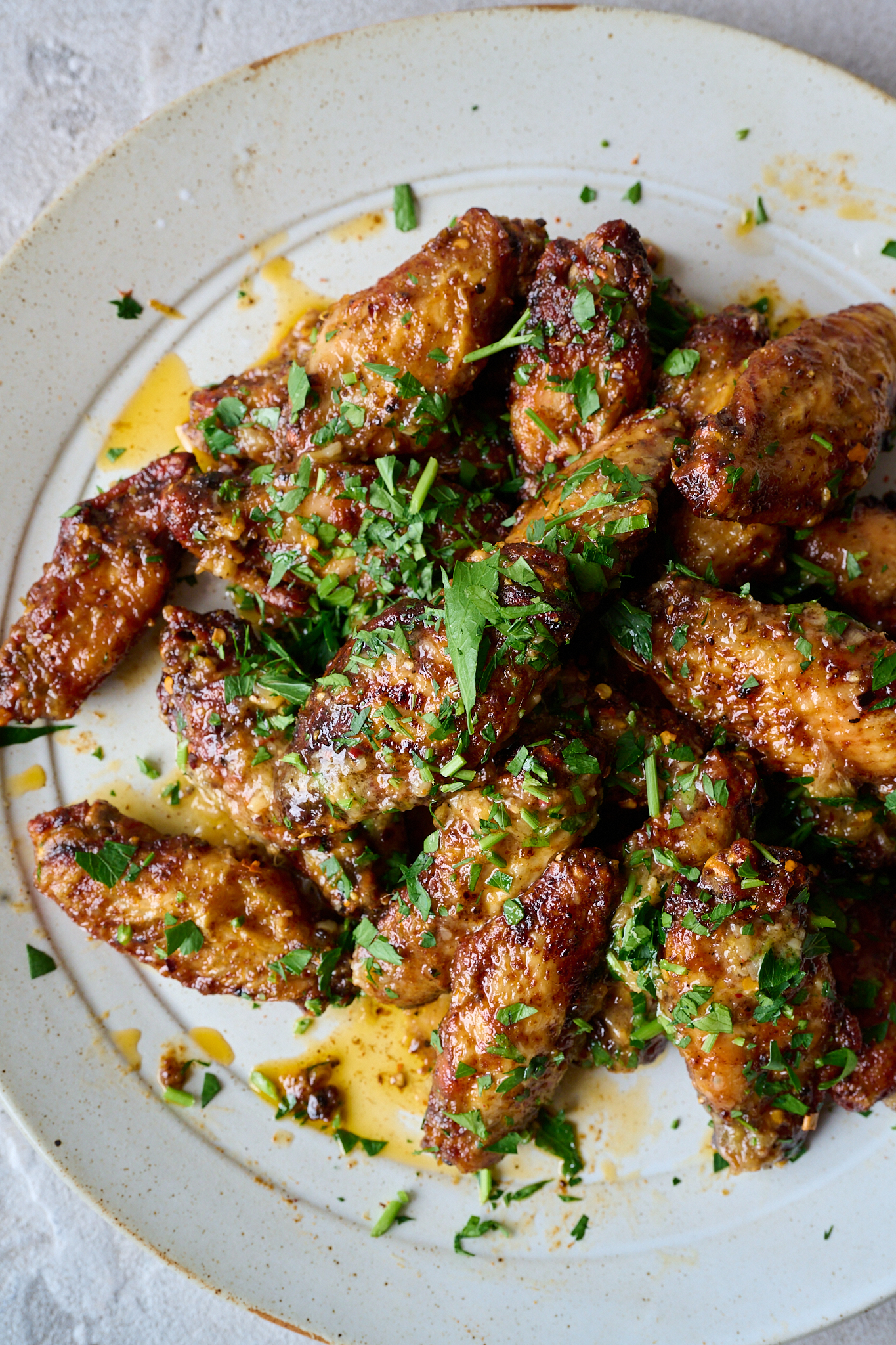 Plate full of chicken wings and topped with fresh parsley.