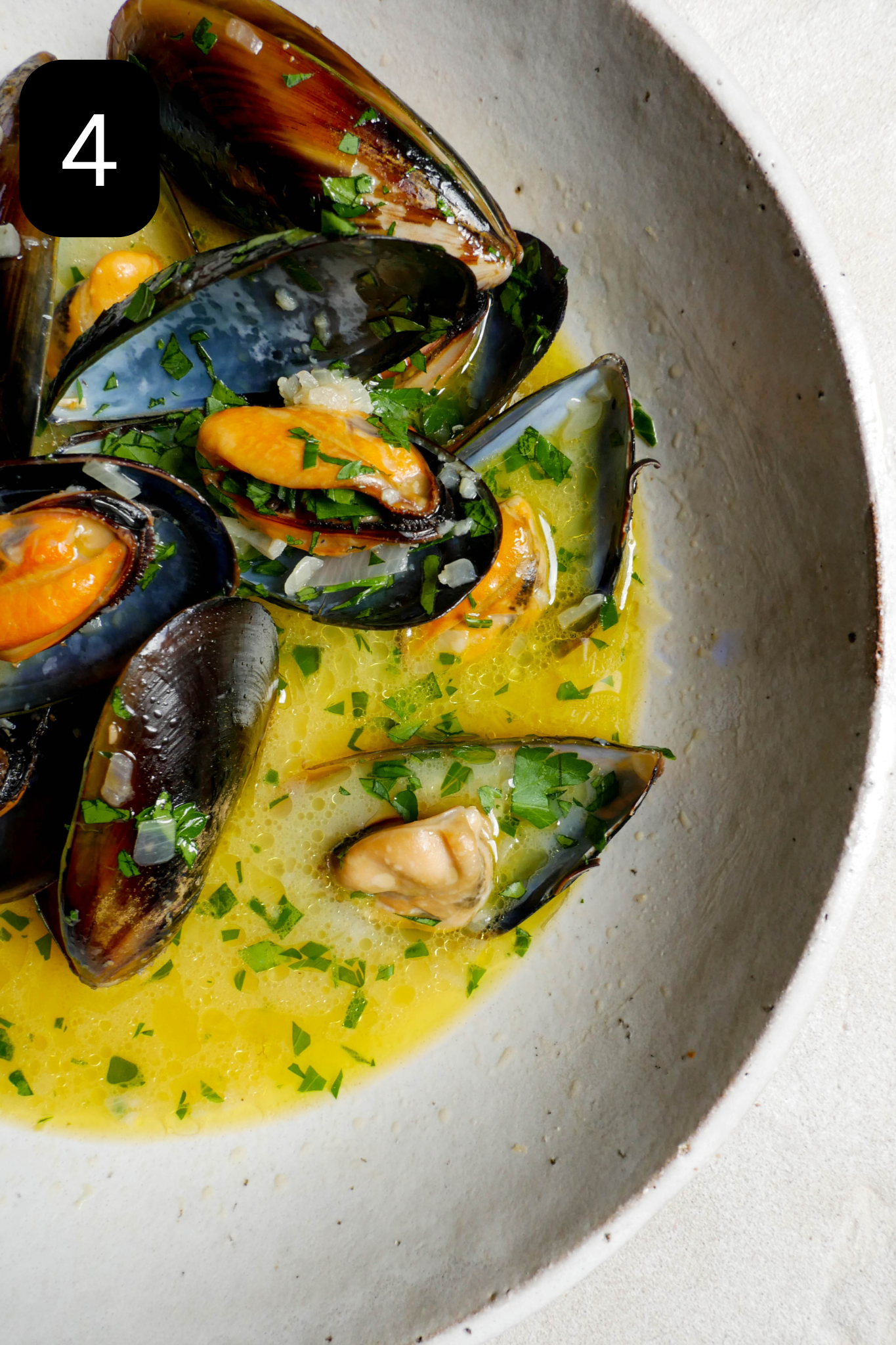 Mussels in large white bowl with sprinkled parsley. 
