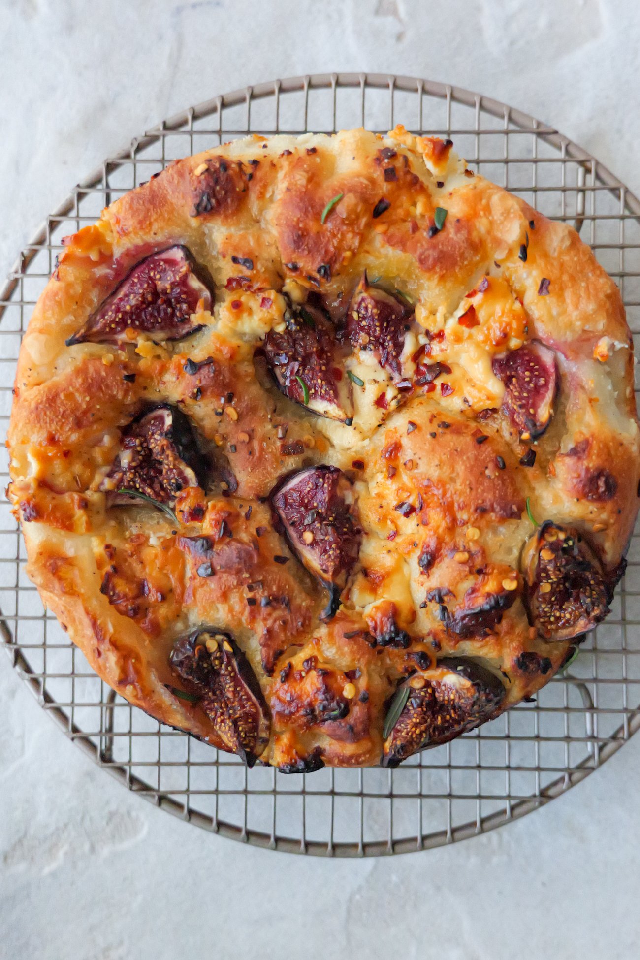 Fig and goats cheese foaccia sits on round metal cooling rack