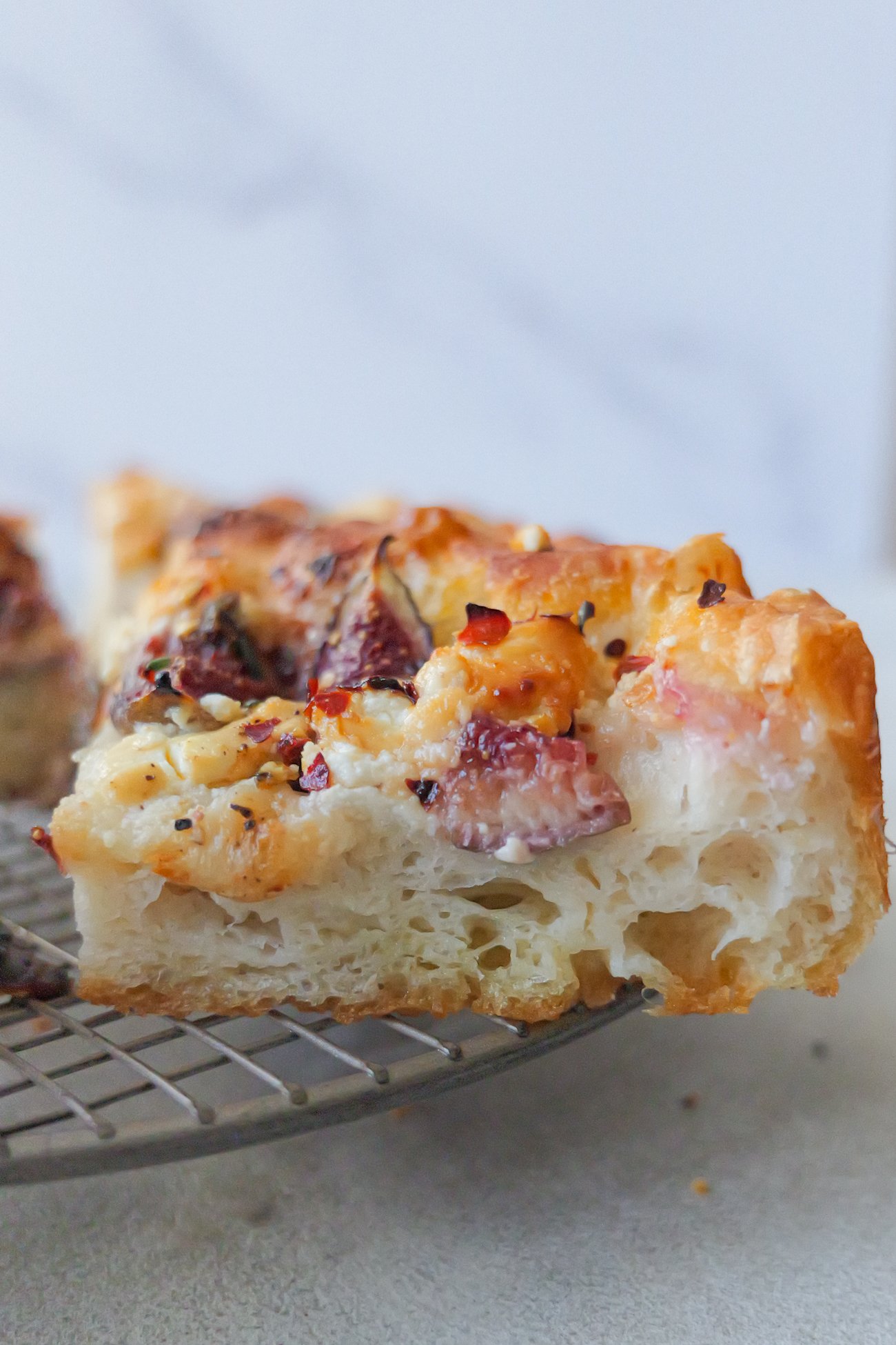 Slice of fig and goats cheese focaccia sitting on metal cooling rack