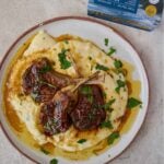 three lamb chops on a pile of mashed potatoes with sauce.