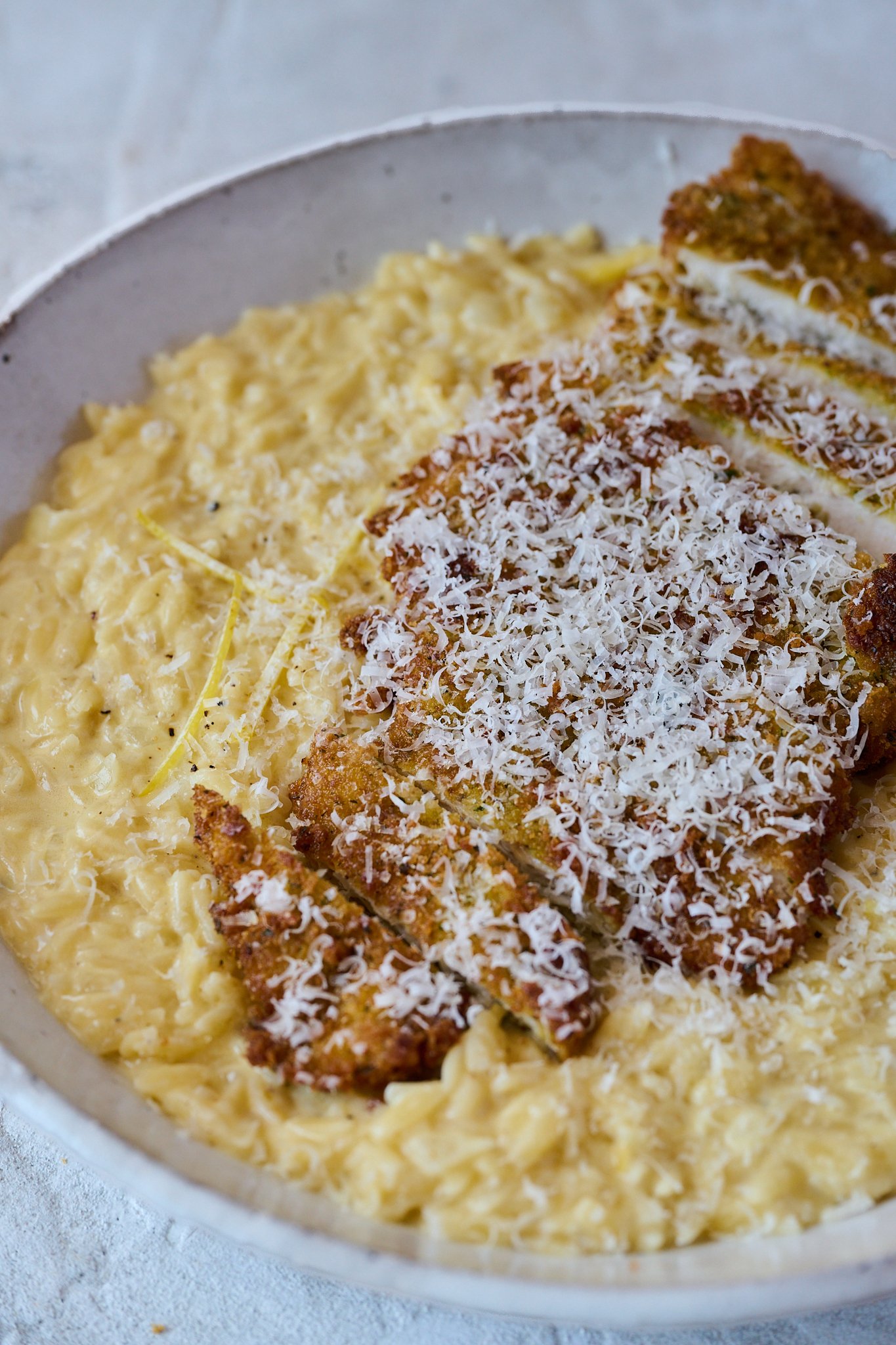 Large white plate filled with lemon orzo and topped with crispy crumbed chicken. Finished with a sprinkling of parmesan cheese. 