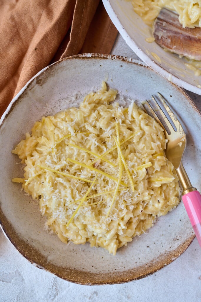 Orzo in brown bowl with orzo and pink fork sticking out the side. Topped with extra lemon zest and parmesan. 