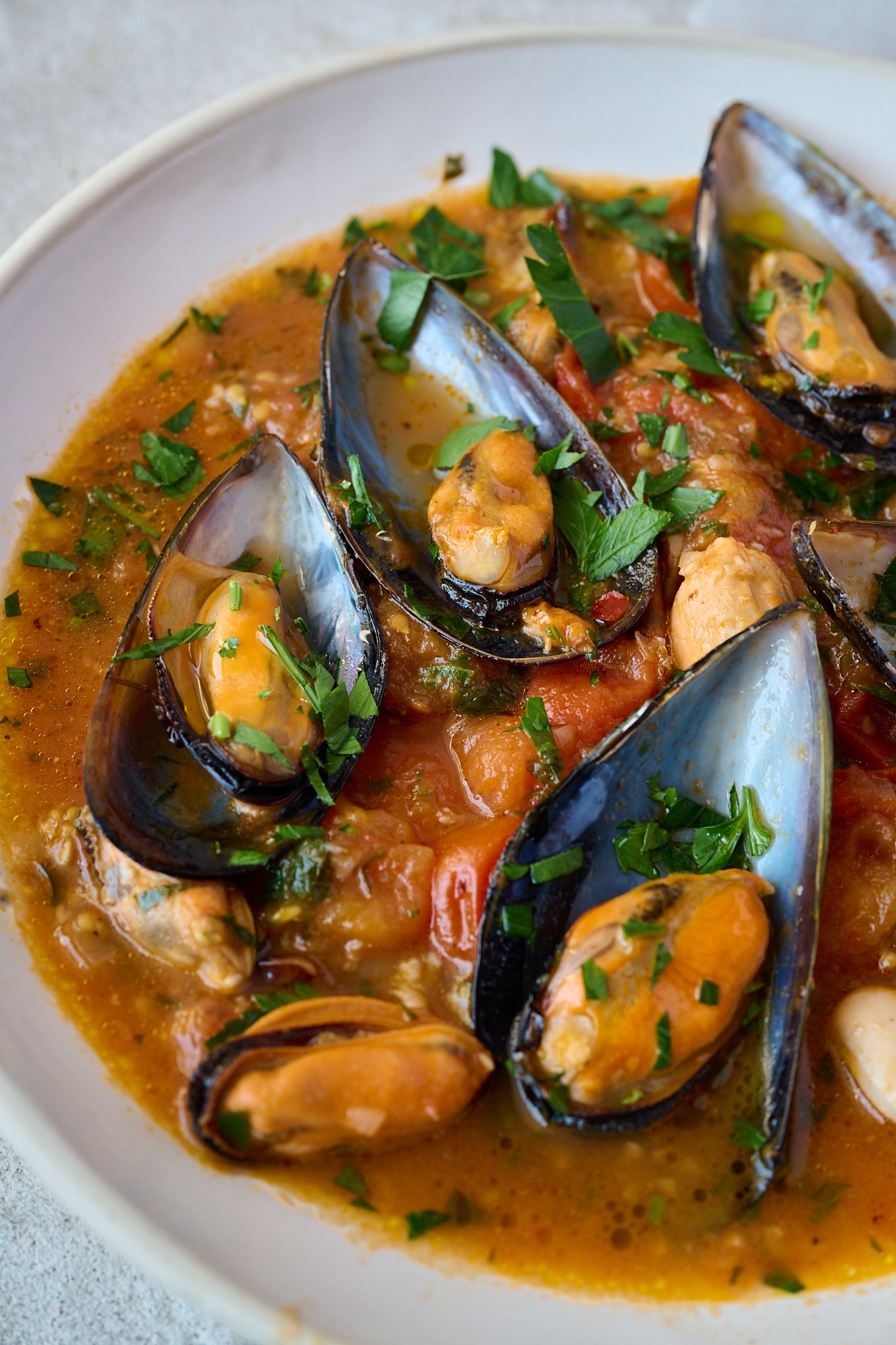 Close up image of cooked mussels in a tomato sauce with fresh parsley sprinkled all over.