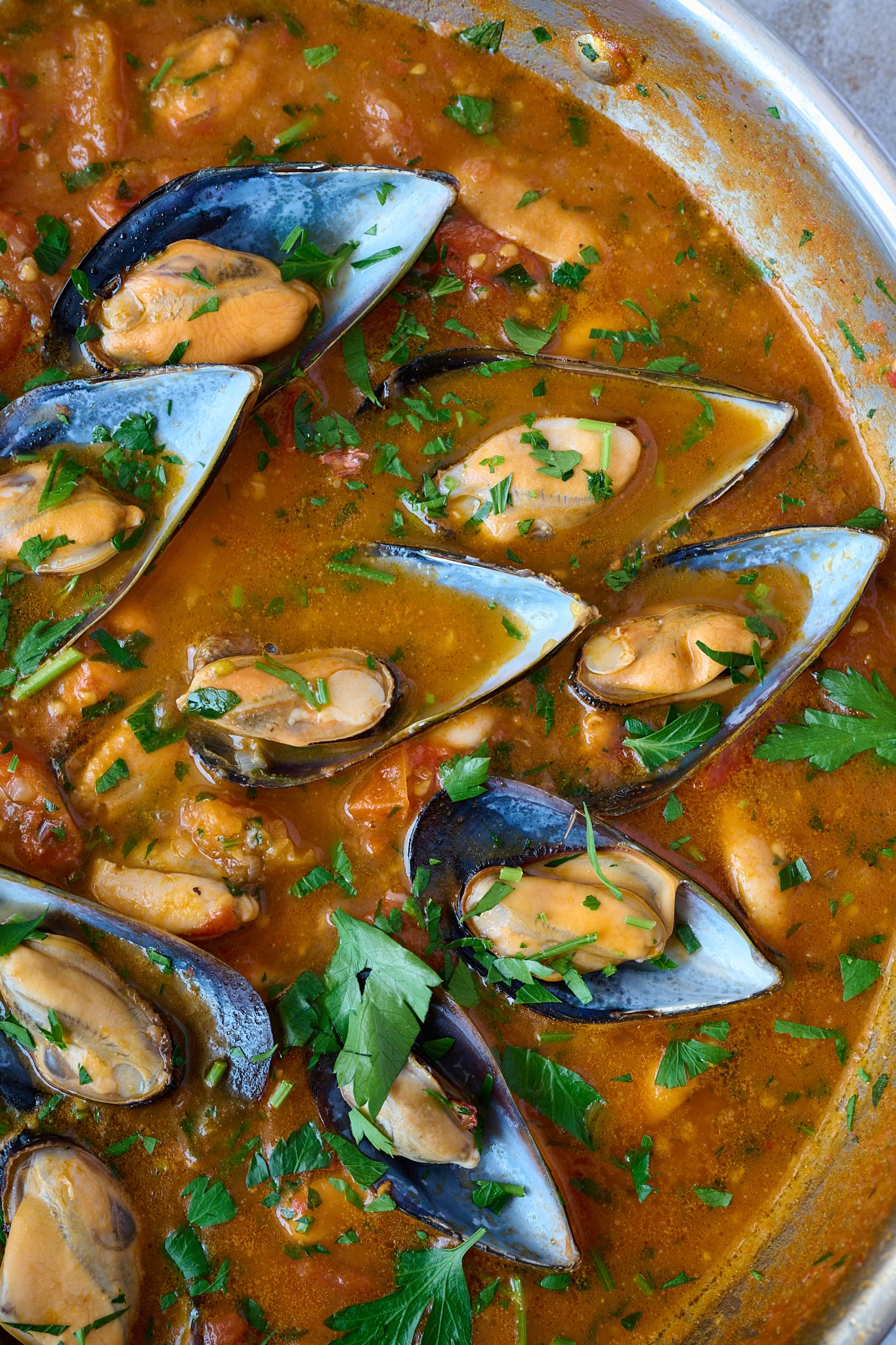 Close up image of cooked mussels in a tomato sauce with fresh parsley sprinkled all over. 