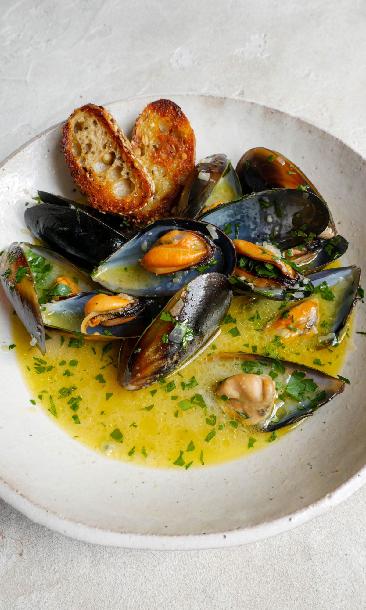 Mussels in large white bowl with two slices of fried baguette. Fresh parsley sprinkled over the top. 