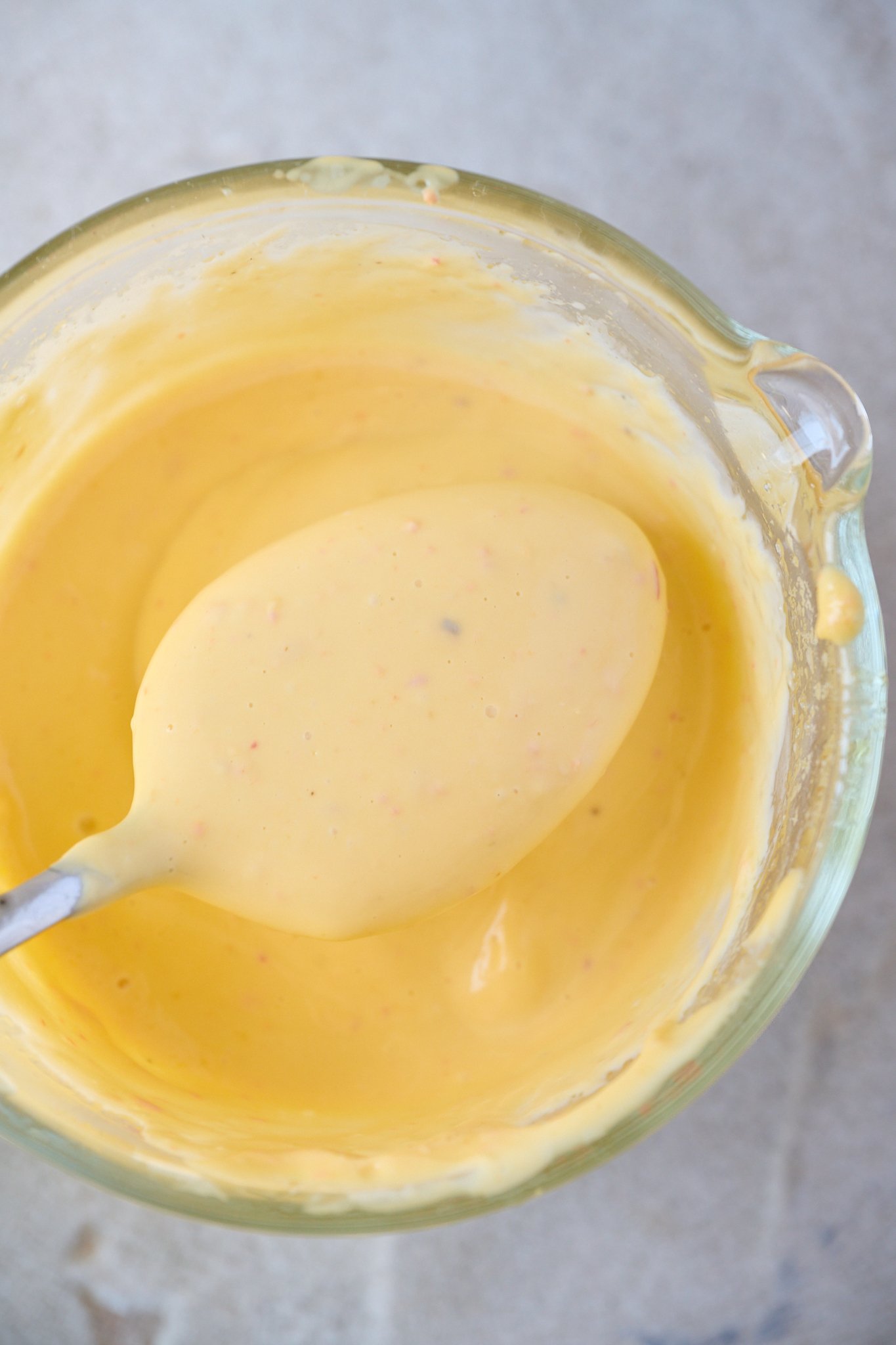 Olive oil mayonnaise is in a glass jar with a spoon in it.
